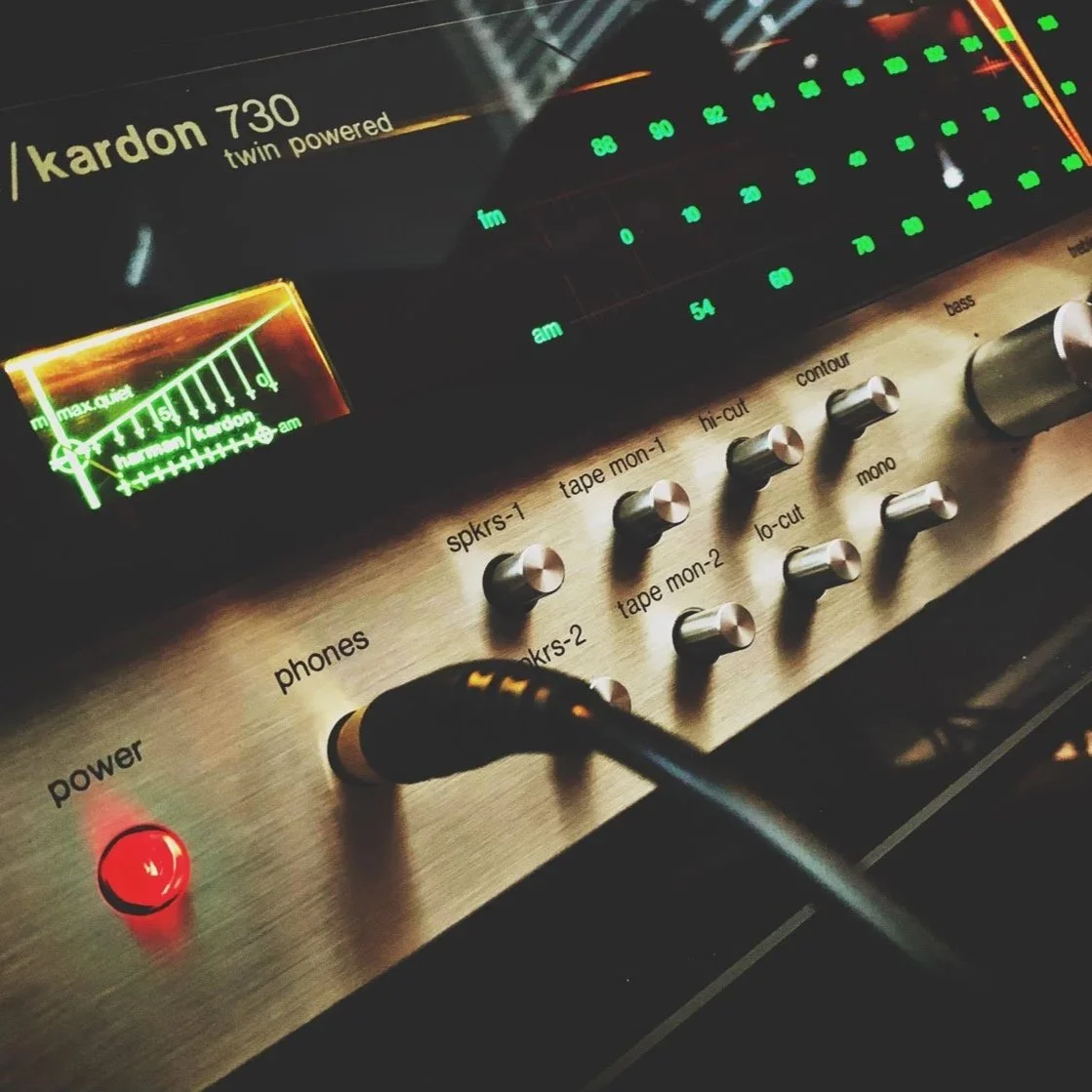 Close-up of a vintage audio mixing console with various knobs labeled for different functions, a power button illuminated red, and a LED display showing audio levels.