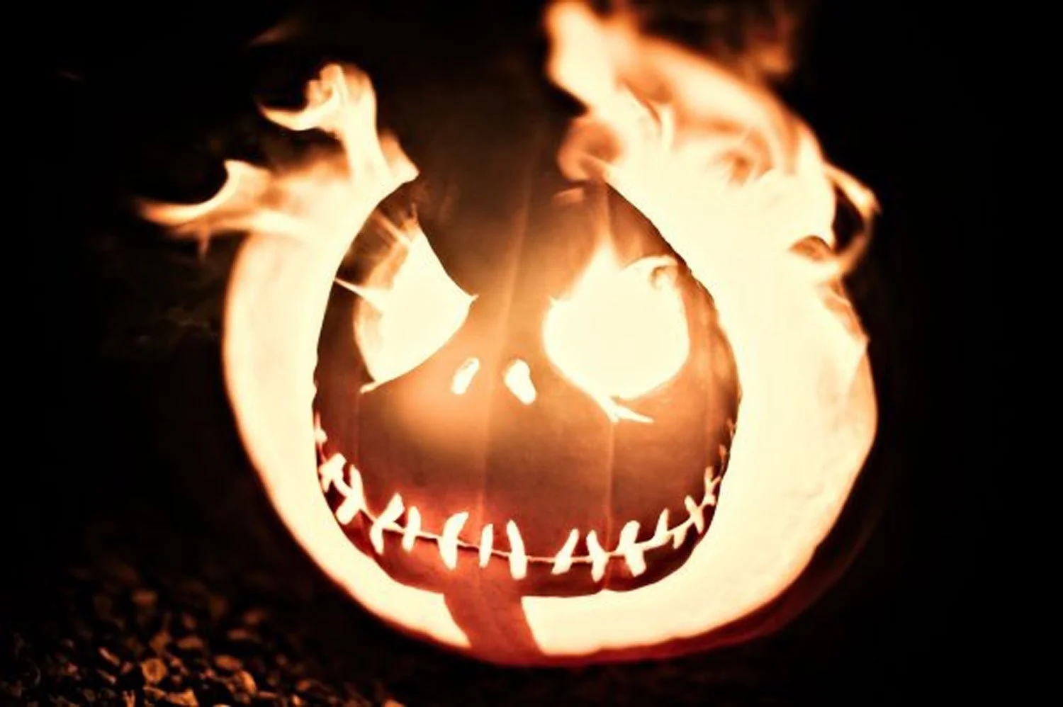 A carved pumpkin with a face design, illuminated from within, with flames coming out of the top.