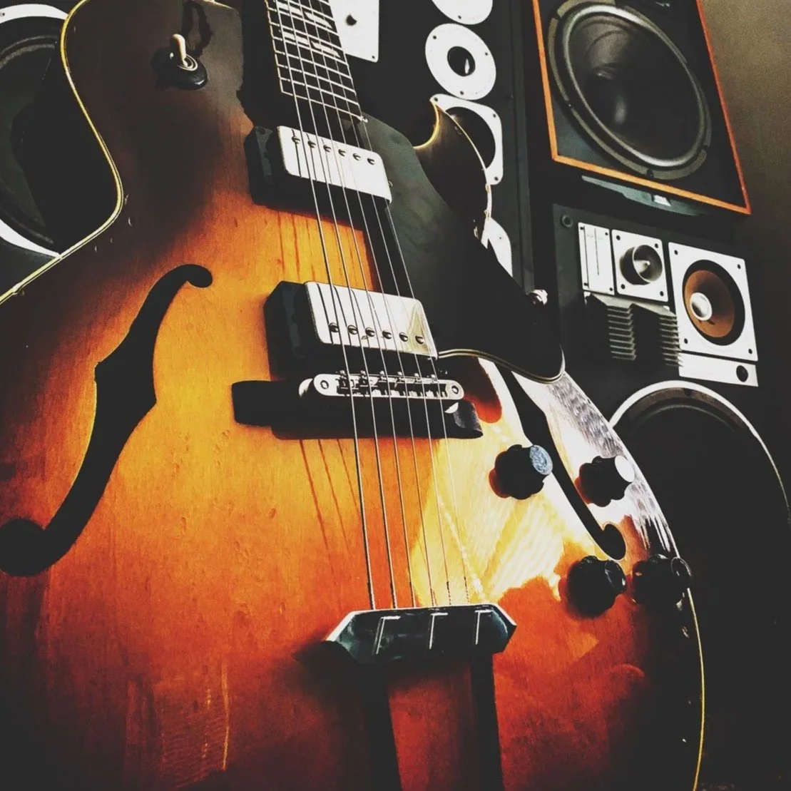 Close-up of an electric guitar with a sunburst finish, placed near studio monitors and speakers.