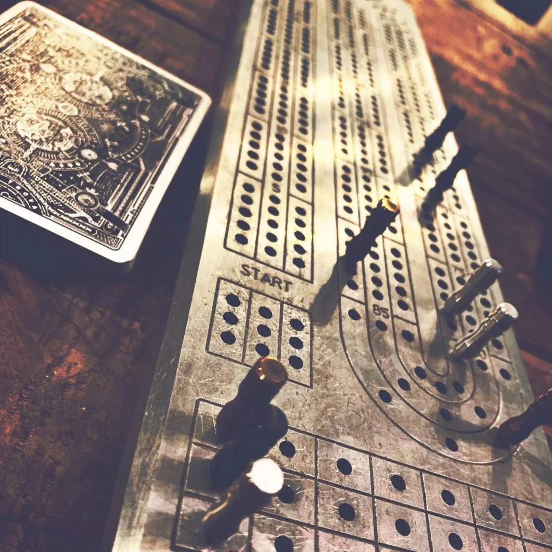A vintage dice game board with metal dice and a deck of playing cards on a wooden surface.
