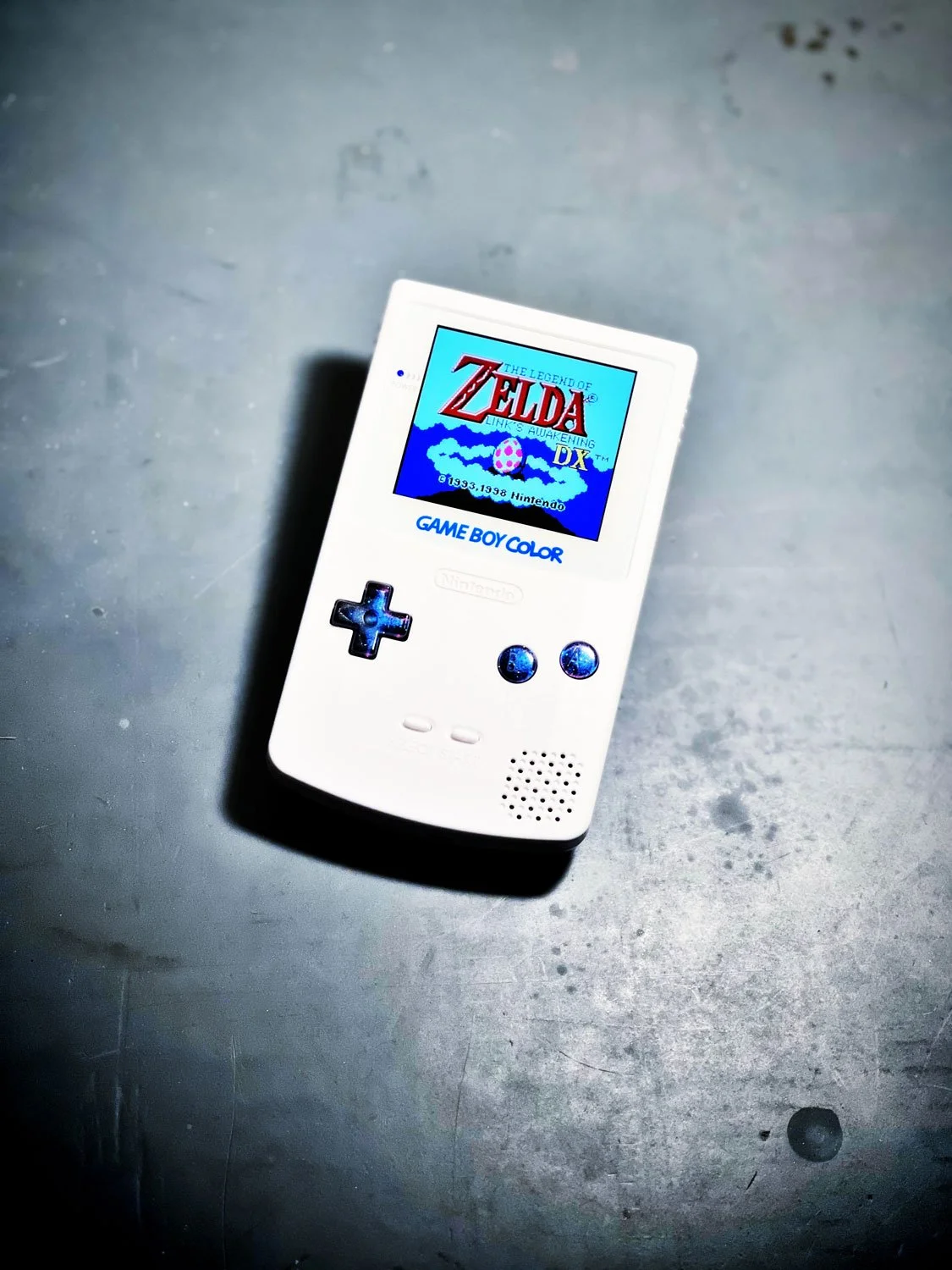 A white Nintendo Game Boy Color handheld gaming device displaying the title screen of The Legend of Zelda: Link's Awakening DX.