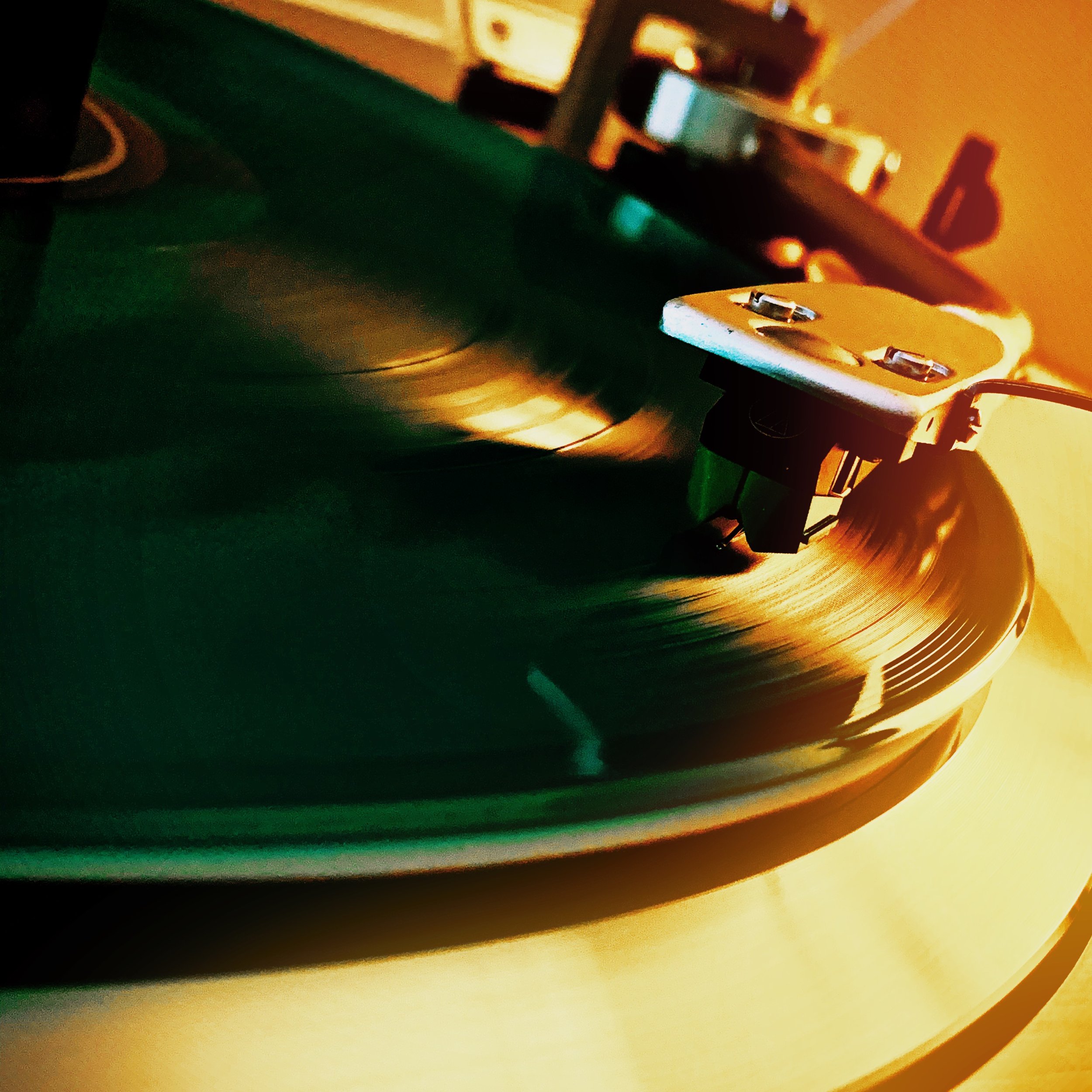 Close-up of a vinyl record spinning on a turntable with a stylus playing the record, illuminated by warm, golden light.
