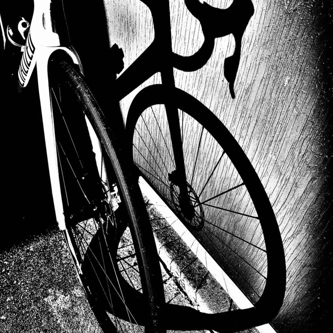 Black and white photo of a bicycle leaning against a textured wall, with the photo taken from a low angle.