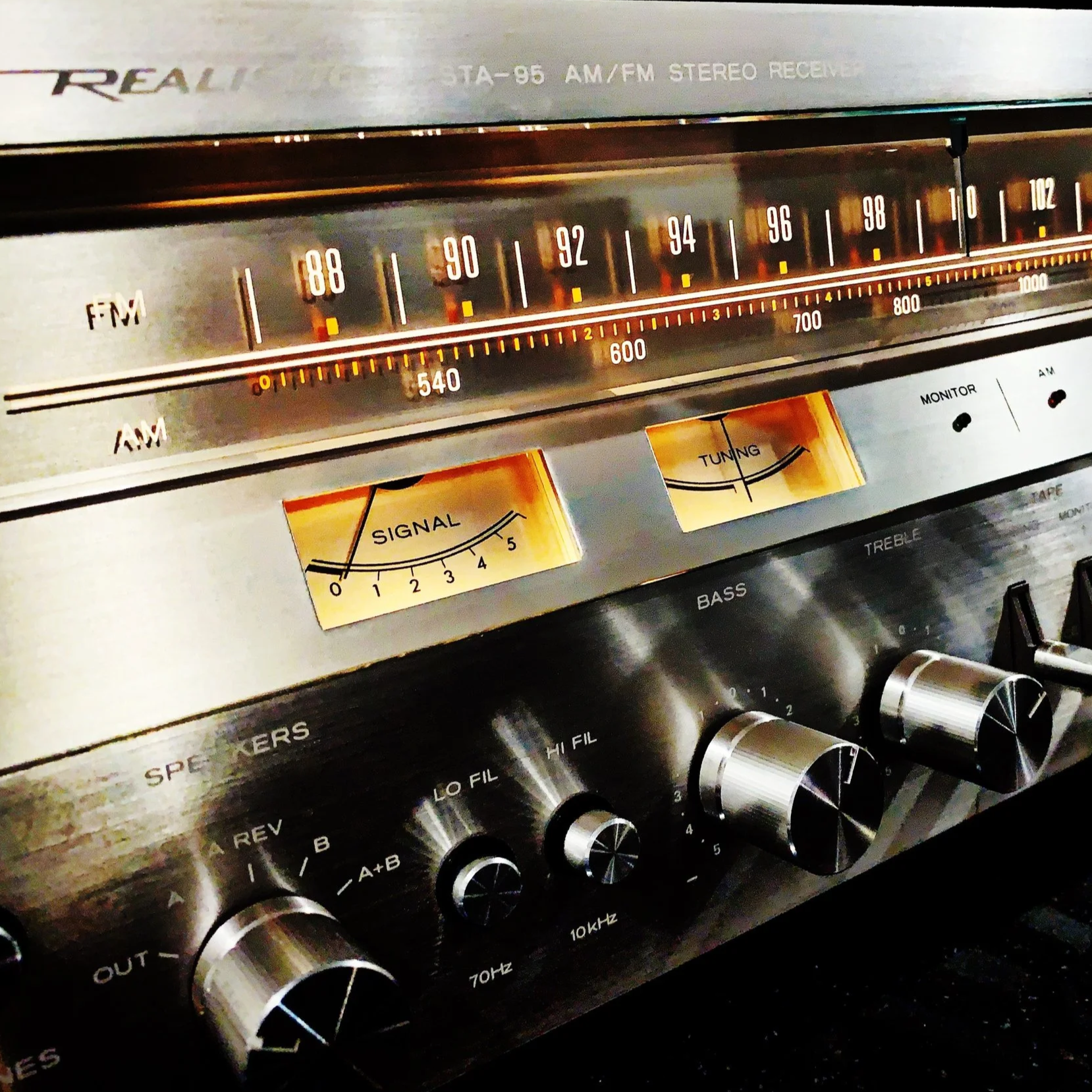 Close-up of a vintage stereo receiver with tuning and signal strength indicators, including knobs for volume, bass, treble, and other audio controls.