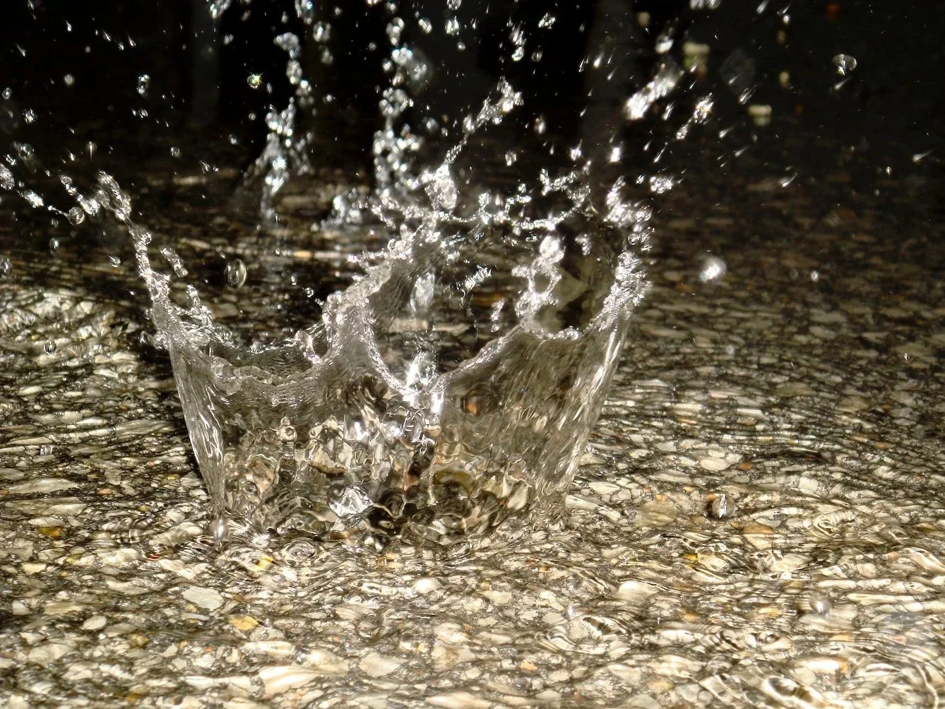 Close-up of water splashing on a pebble-covered surface, captured at high speed with reflections and motion details.