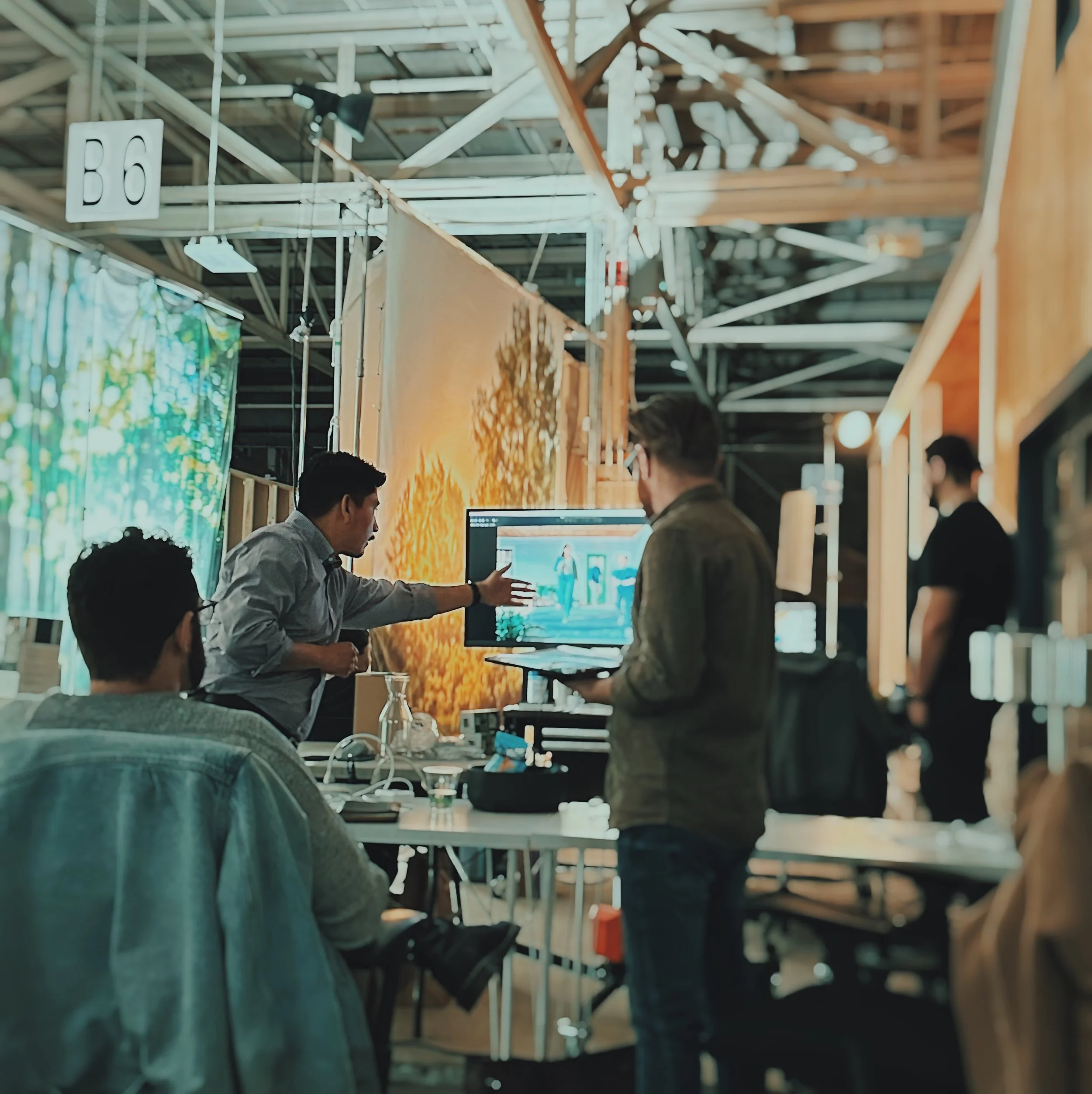 People working at a computer station in an indoor setting with shelves and a sign that reads 'B6' overhead.