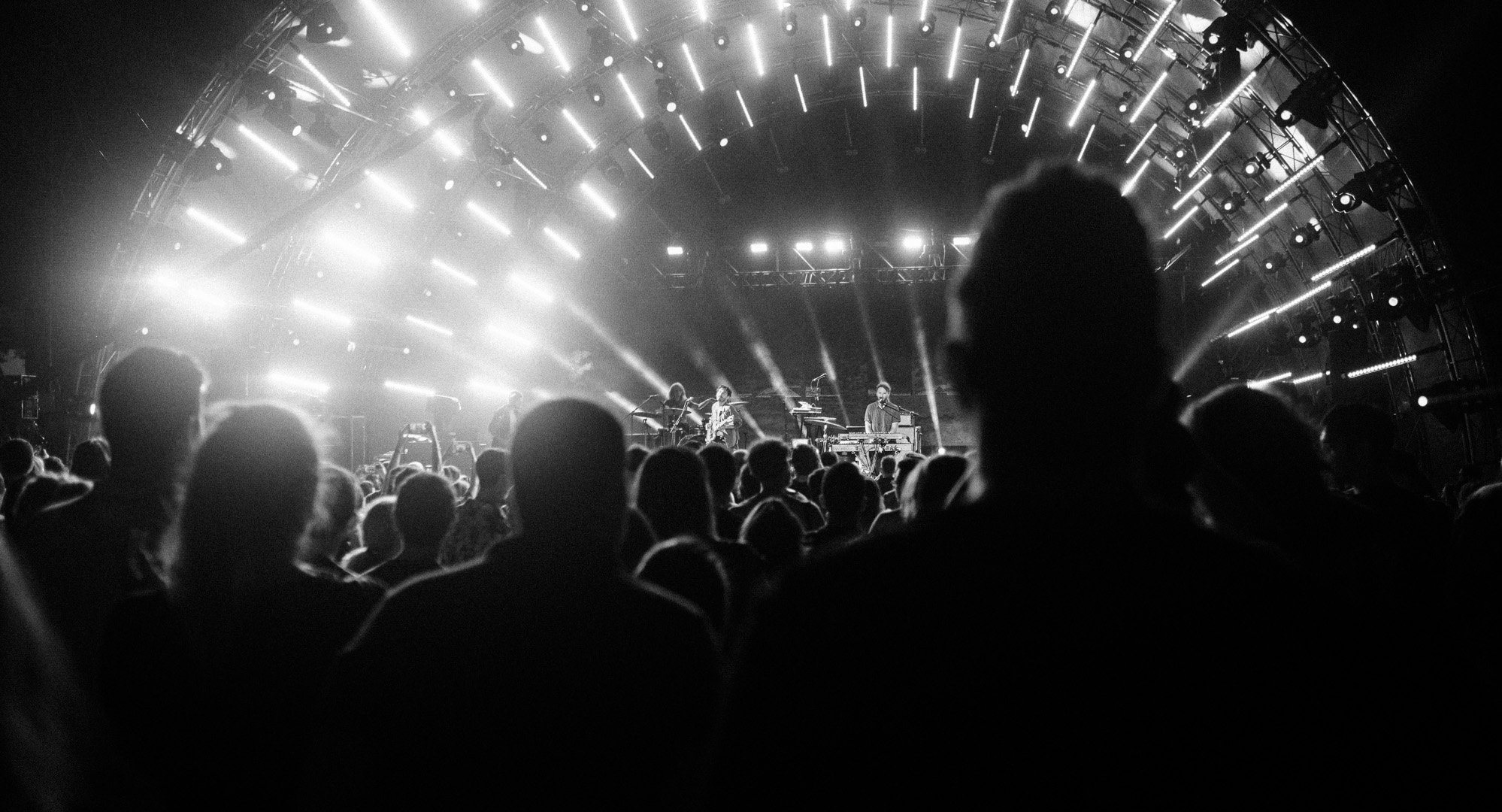 En svart-hvitt konsertscene med mange mennesker i publikum og en band på scenen med lys og utstyr.
