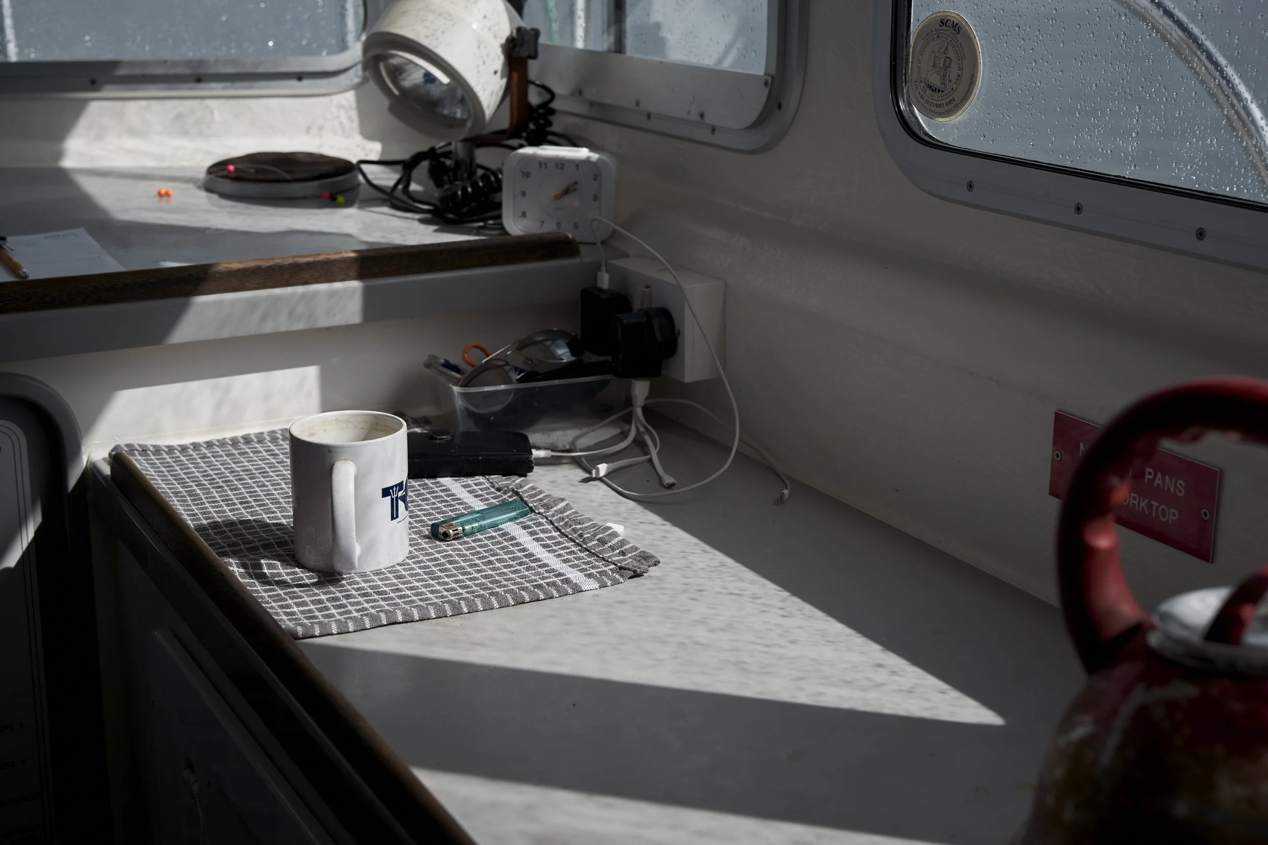 A cluttered boat interior with a coffee mug, a lighter, a pen, sunglasses, cords, a clock, and a red fire extinguisher.