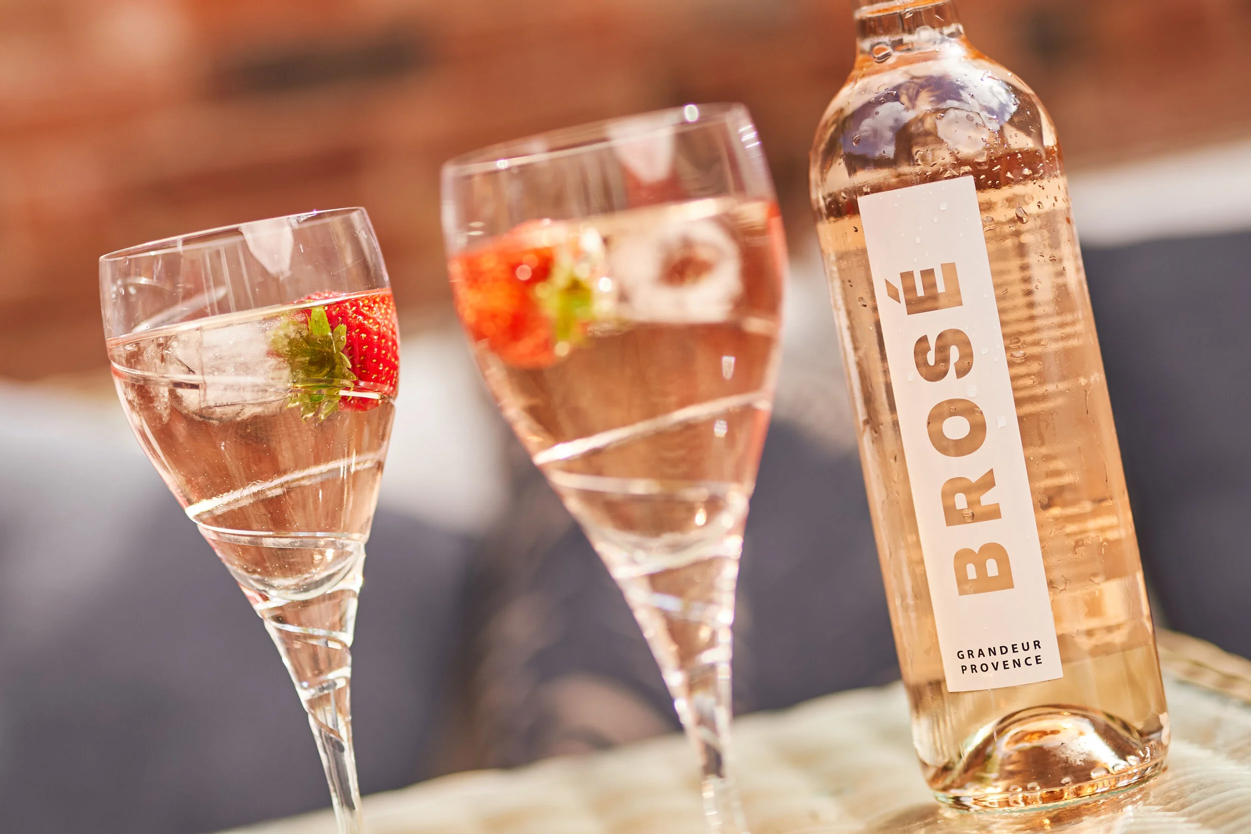 A bottle of rosé wine and two wine glasses with rosé and strawberries on a table.