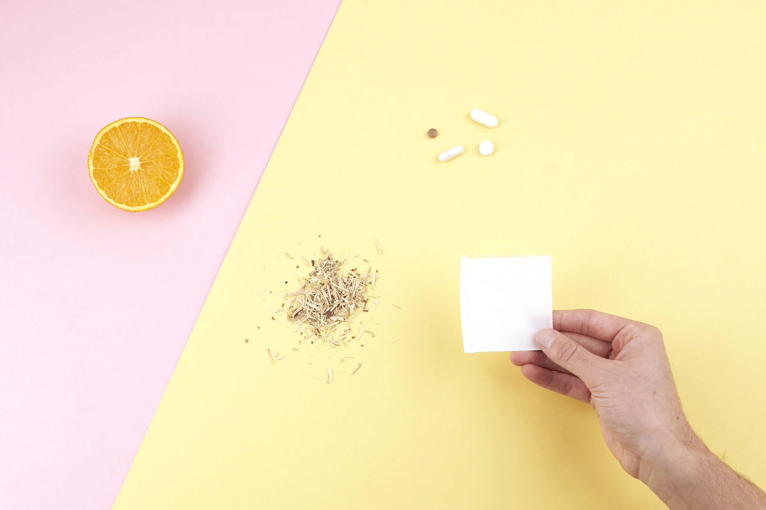 A half orange on a pink background, various pills and herbs on a yellow background, and a hand holding a white square piece of paper.
