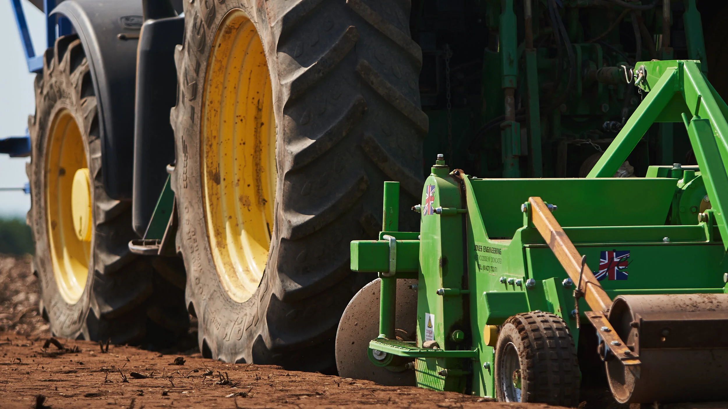 Close-up of large tractor tires with a green soil roller in front, working on dirt in an agricultural field.
