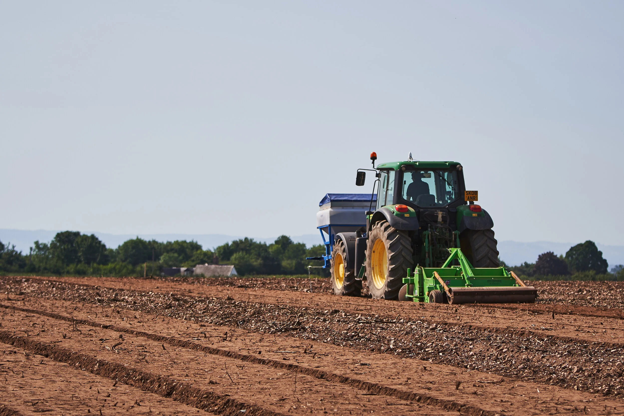 A tractor working on a field with barren soil and distant trees on a clear day.