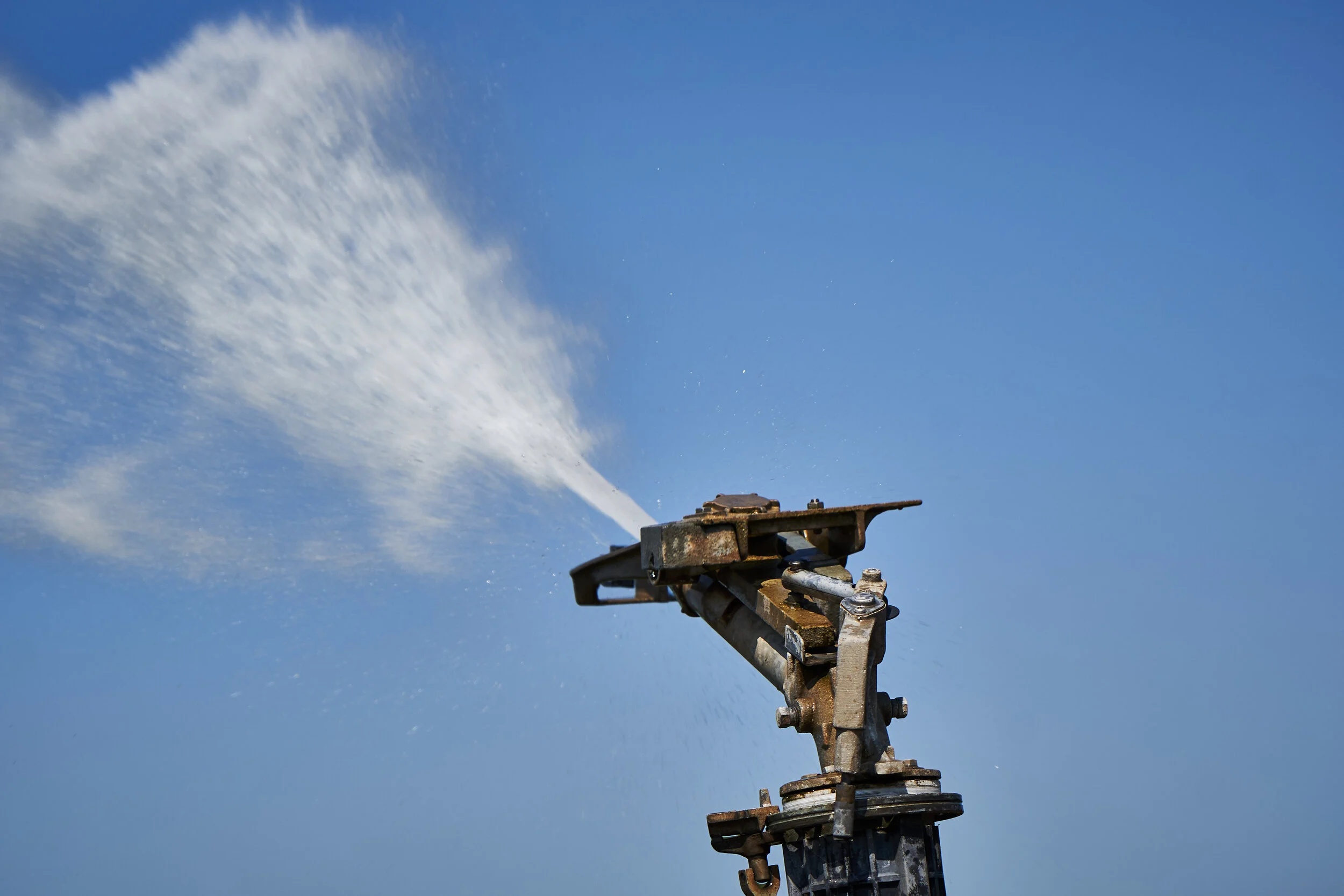 A rusty metal fire hydrant spraying water against a clear blue sky.