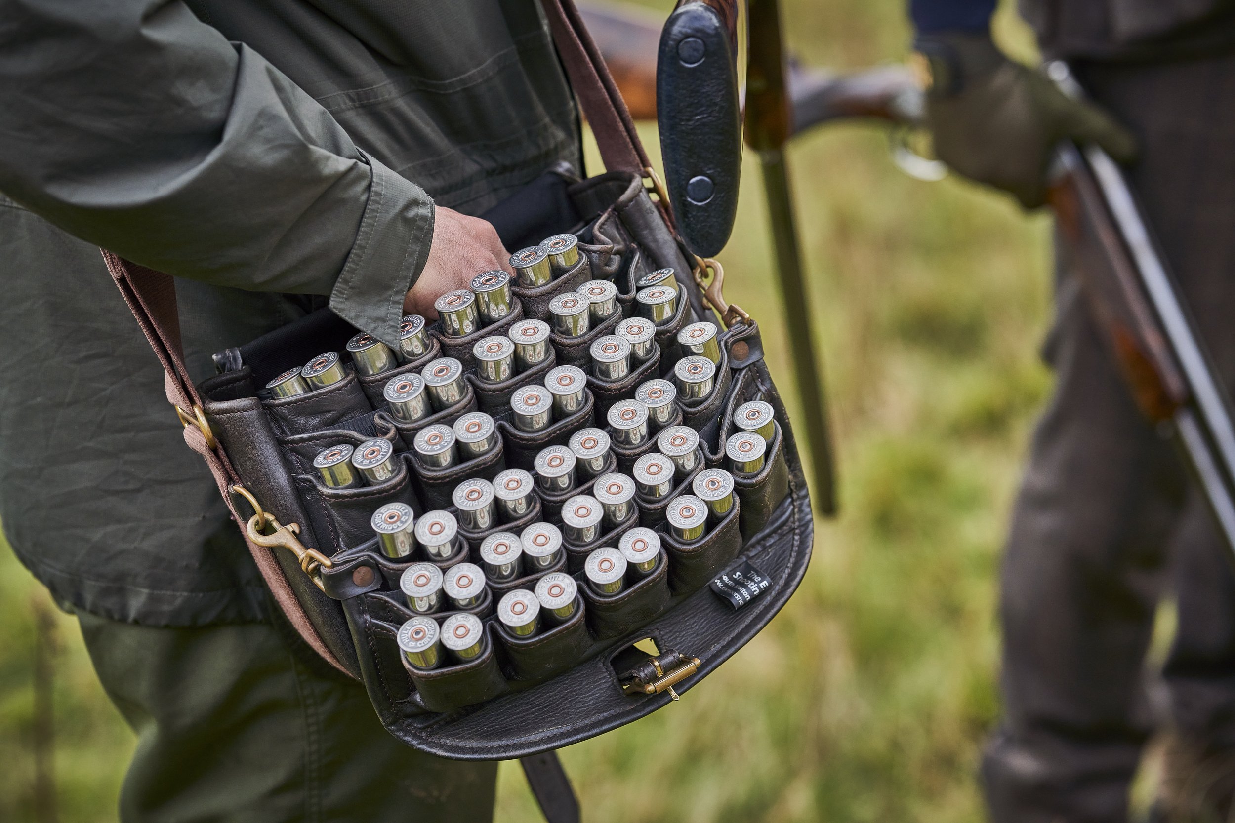 Person holding a leather case filled with shotgun shells outdoors