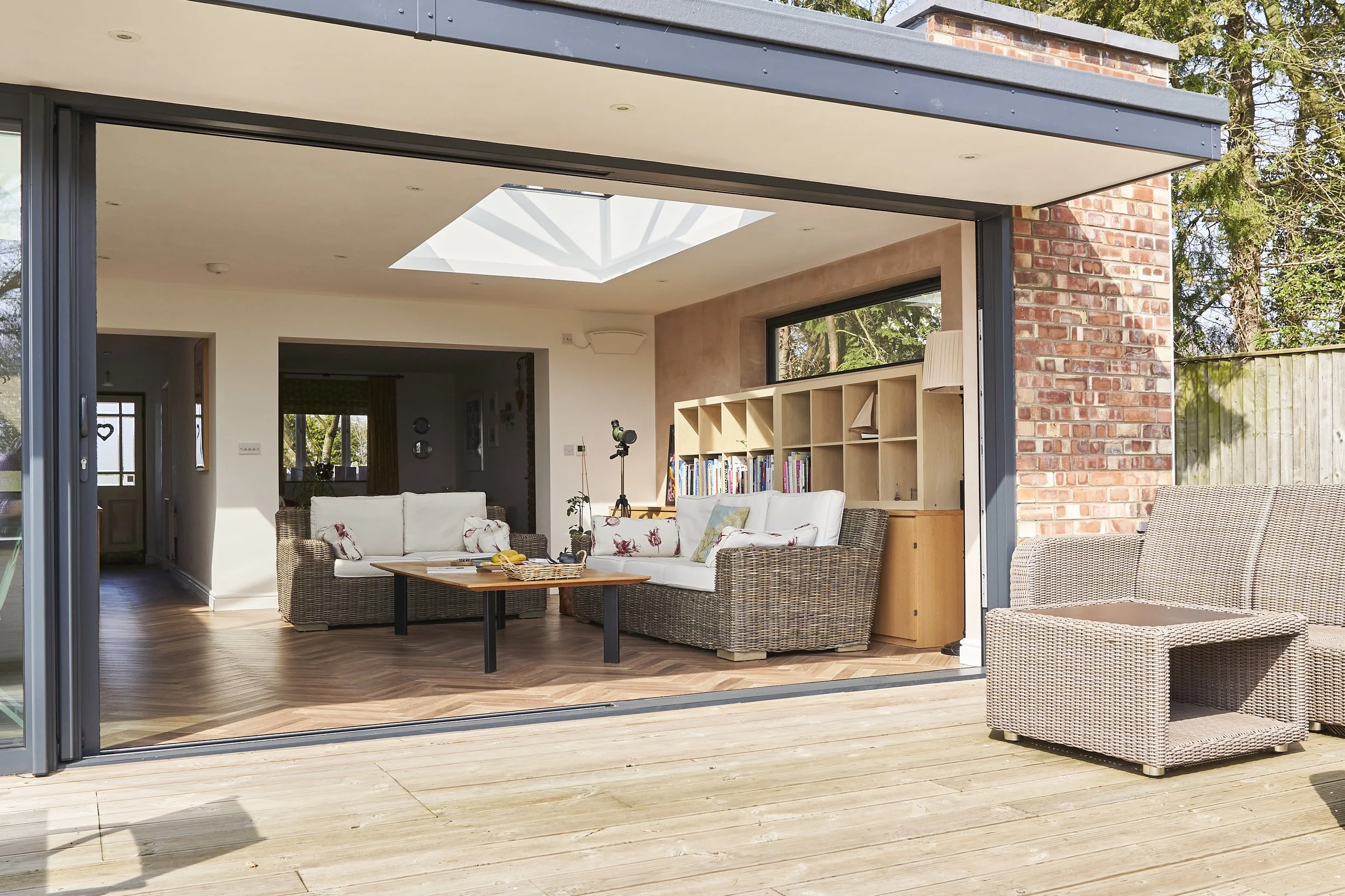Living room with open sliding doors to outdoor wooden deck, wicker outdoor furniture, and bookshelves