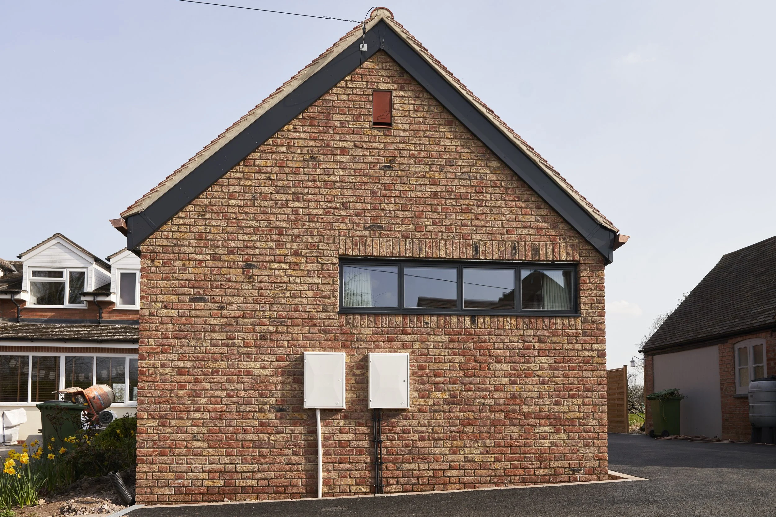 Back of a brick house with a gable roof, a horizontal window, and two electrical boxes on the wall.