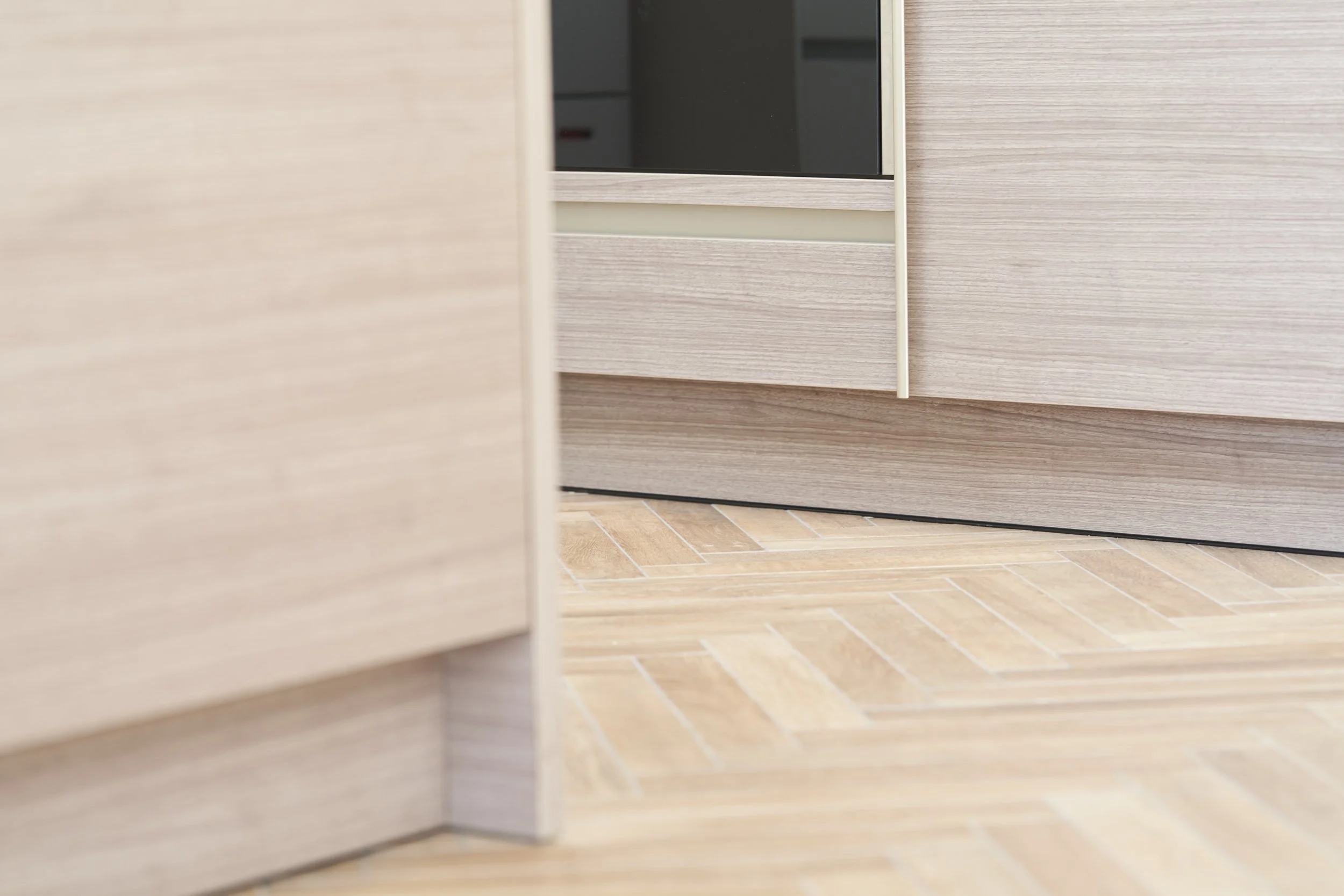 Close-up of the bottom corner of kitchen cabinets and a sliding door with a wooden floor.