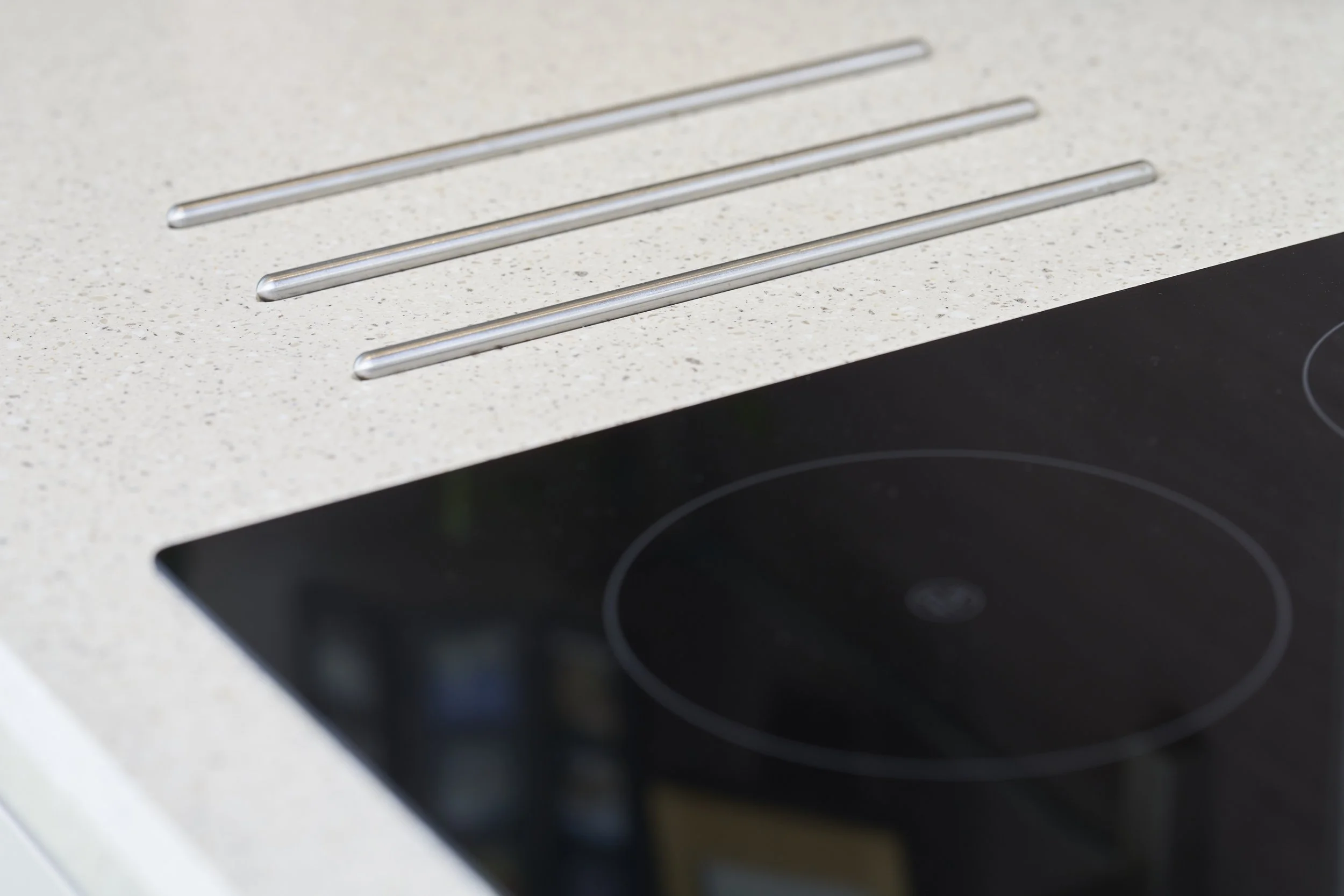 Close-up of a cream-colored kitchen countertop with three metal stove heating element rods and part of a black electric stovetop.