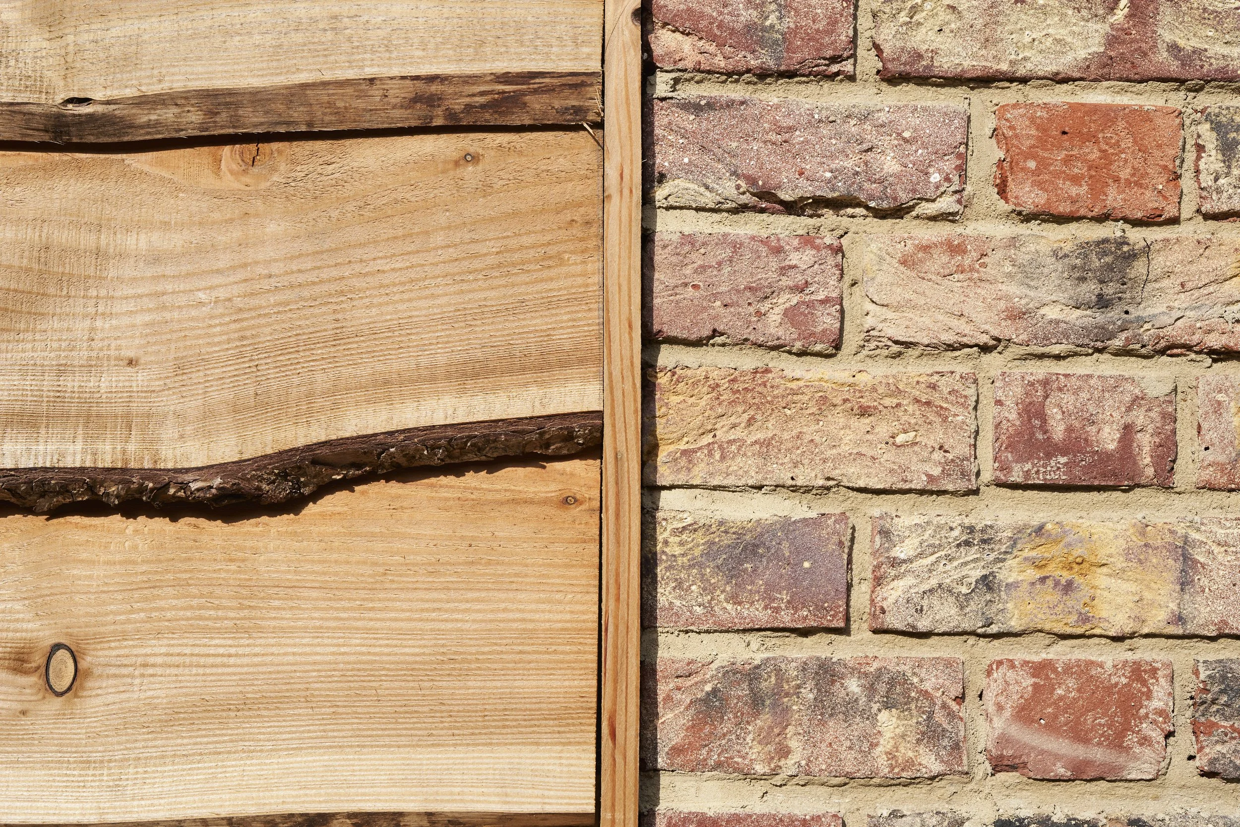 Close-up of a section of a wall with wood on the left side and red brick on the right side.