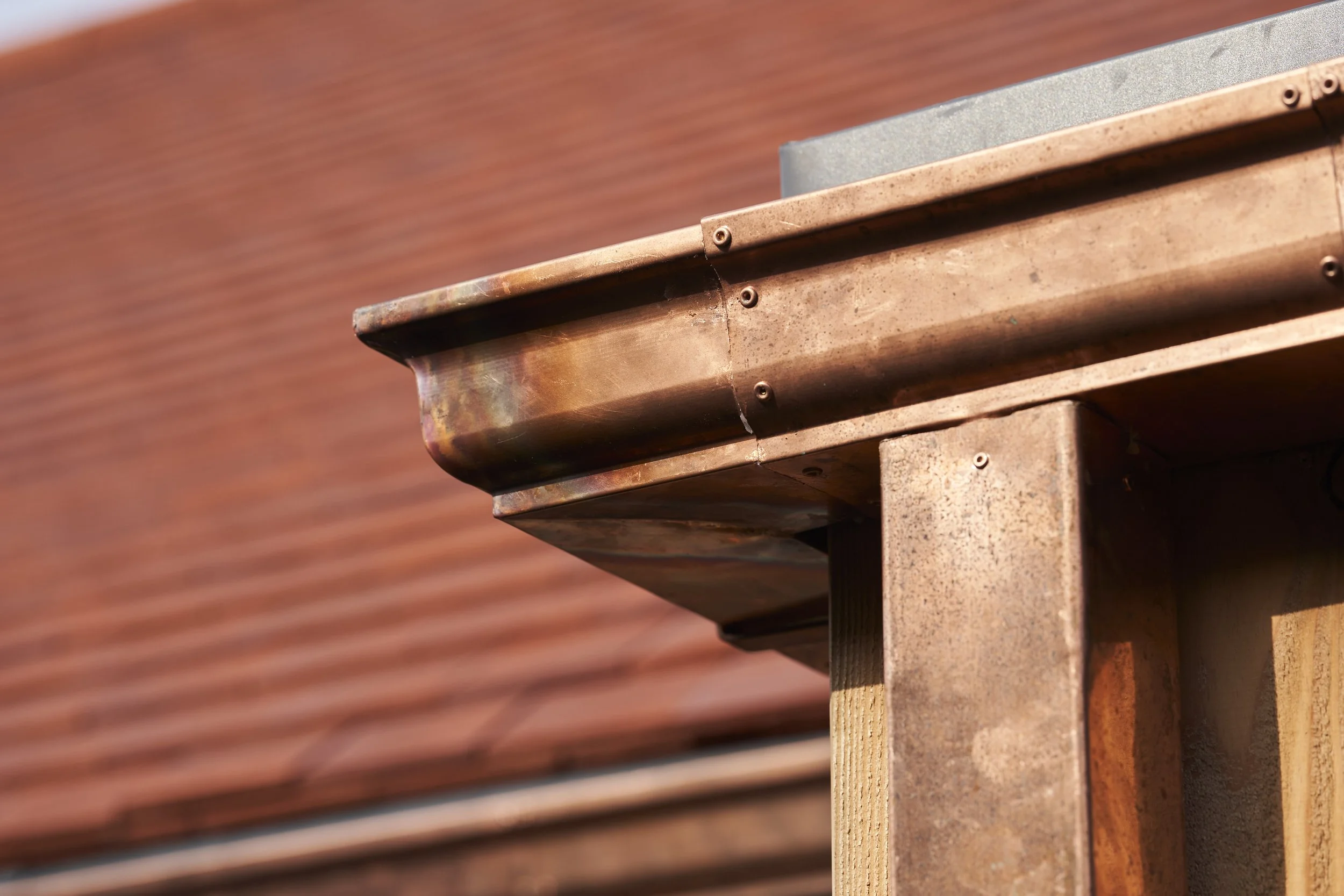 Close-up of a metal roof edge on a wooden structure with a reddish-brown background.