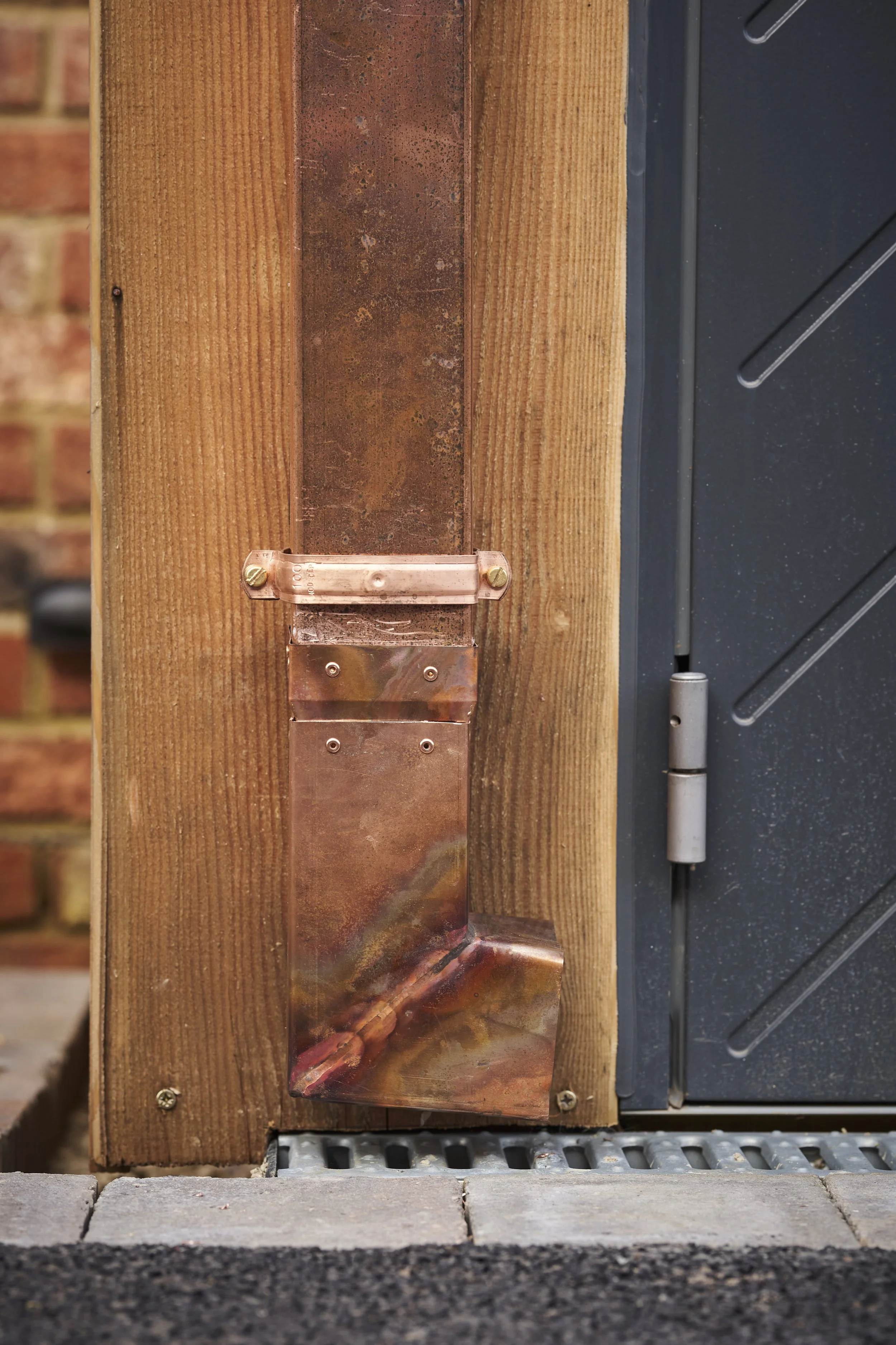 Close-up of a house exterior corner with wooden framing, metal flashing, and a black door hinge on a stress-treated wood post.
