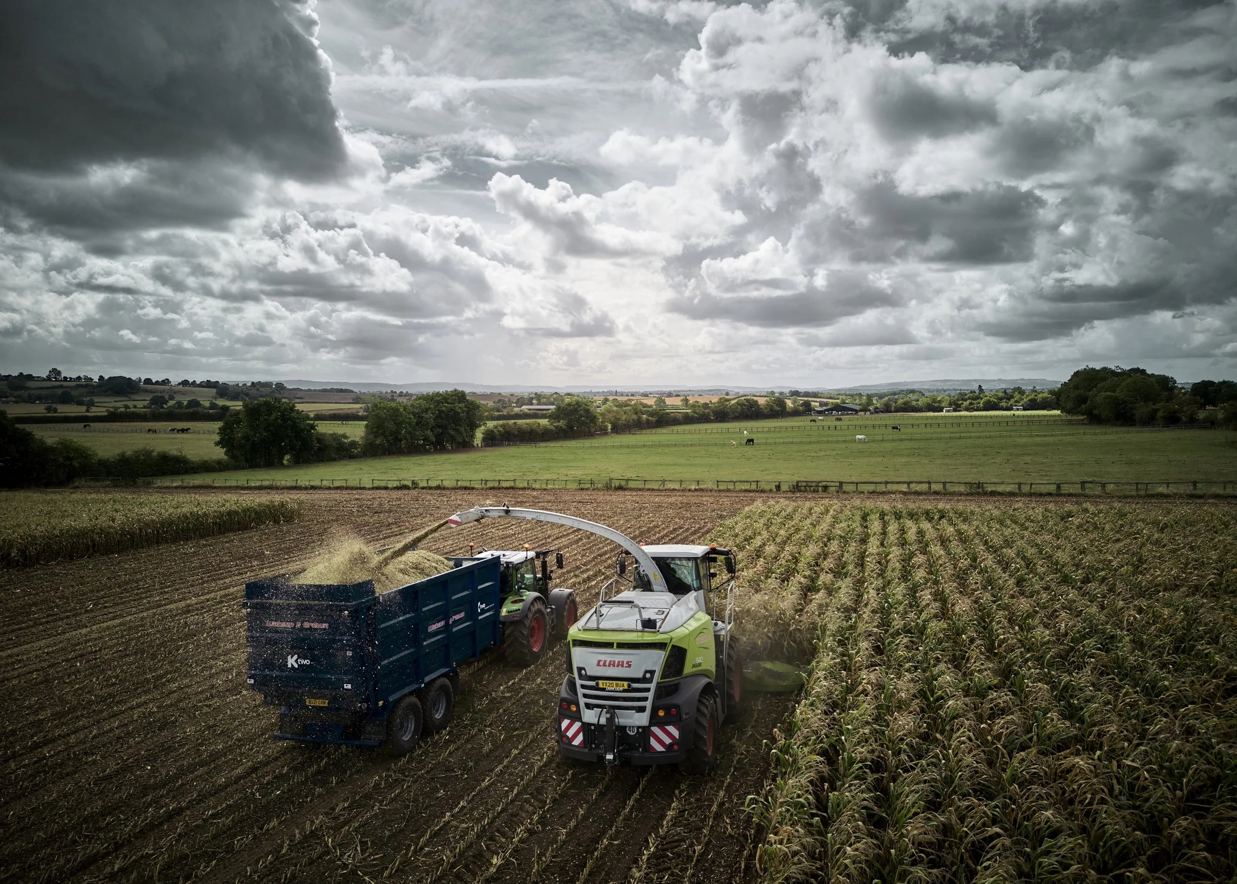 Farmers using machinery to harvest crops in a field beneath a cloudy sky.