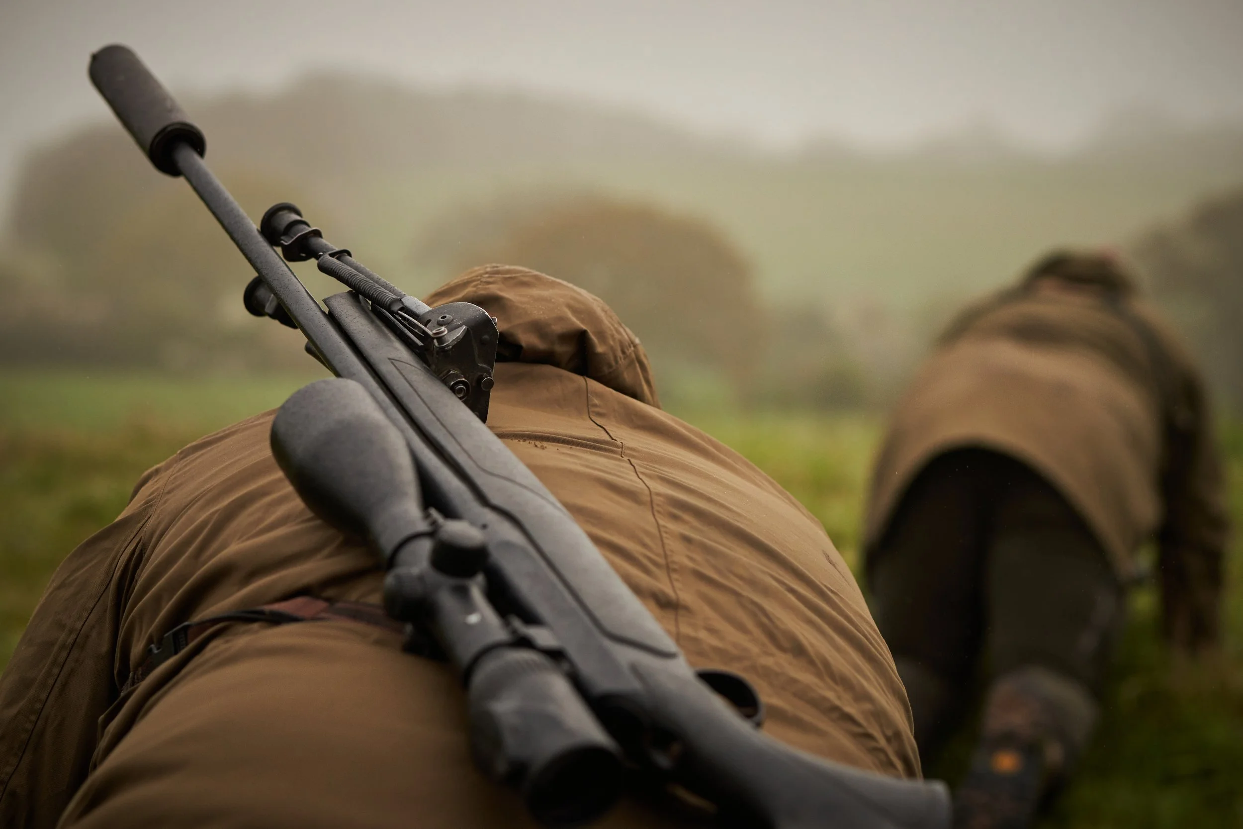 Soldiers crawling on the ground in camouflage gear during foggy weather, with rifles carried along.