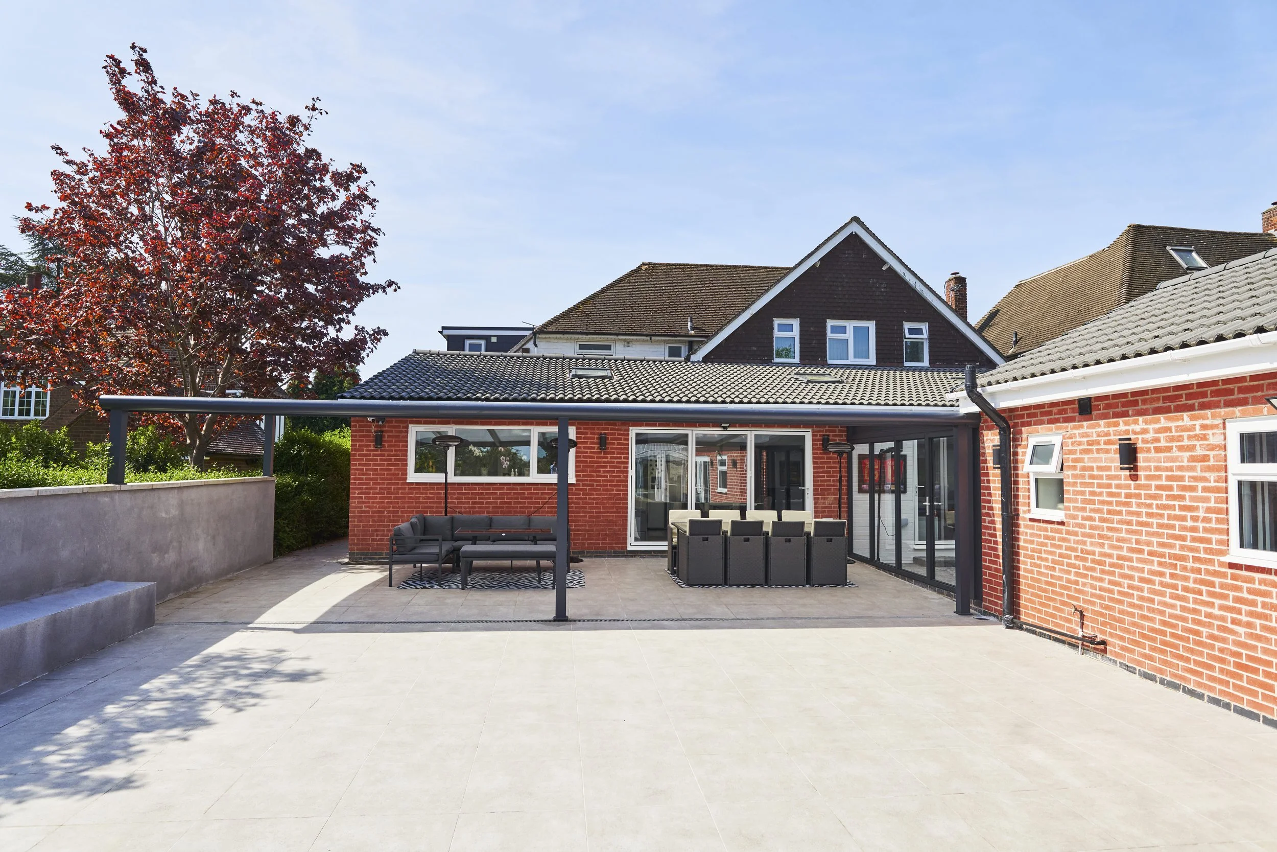 Modern backyard patio with outdoor seating, dining area, and a house with brick exterior and glass sliding doors.