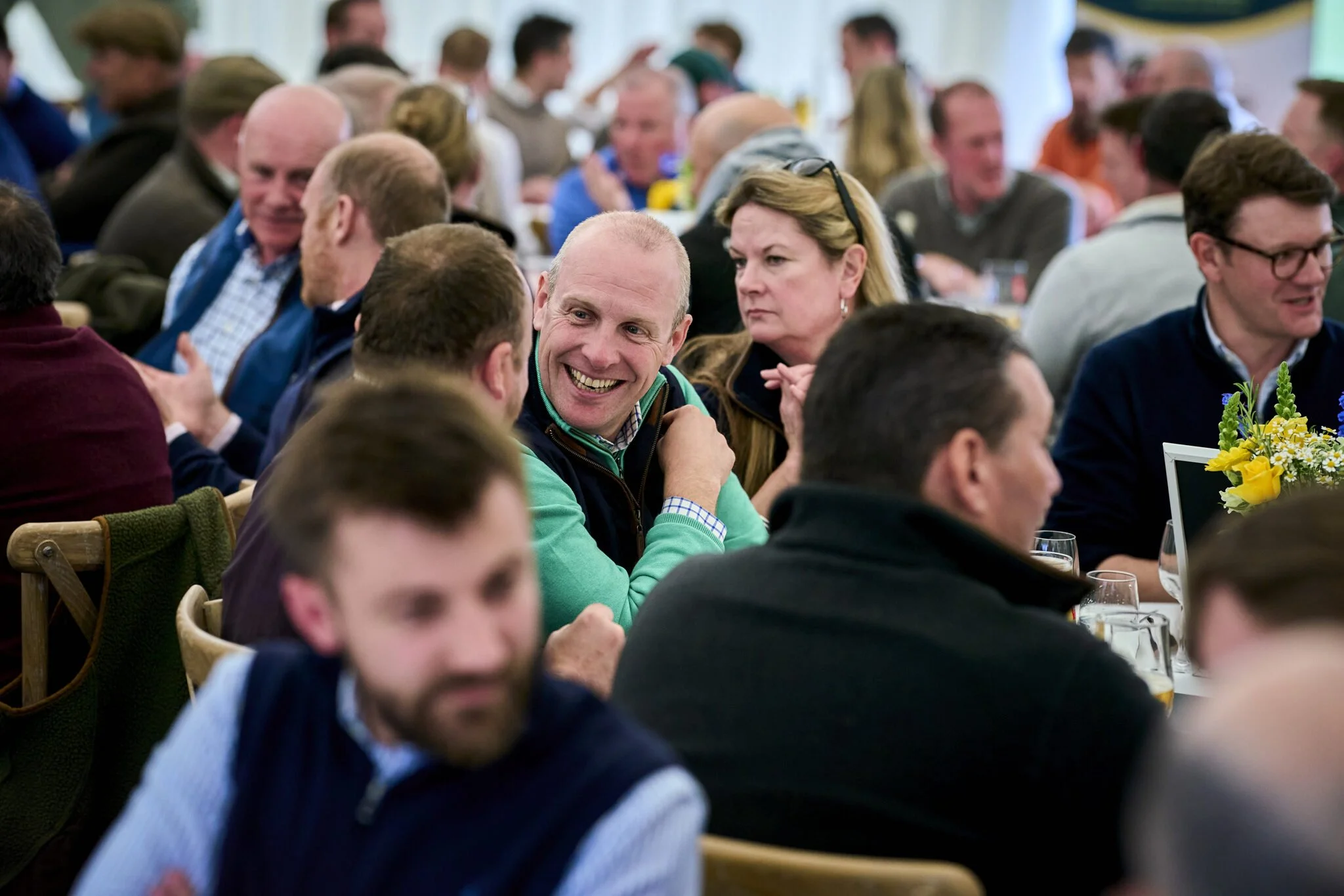 A group of people sitting at a table during a social event, engaging in conversations, with some smiling and others listening attentively.