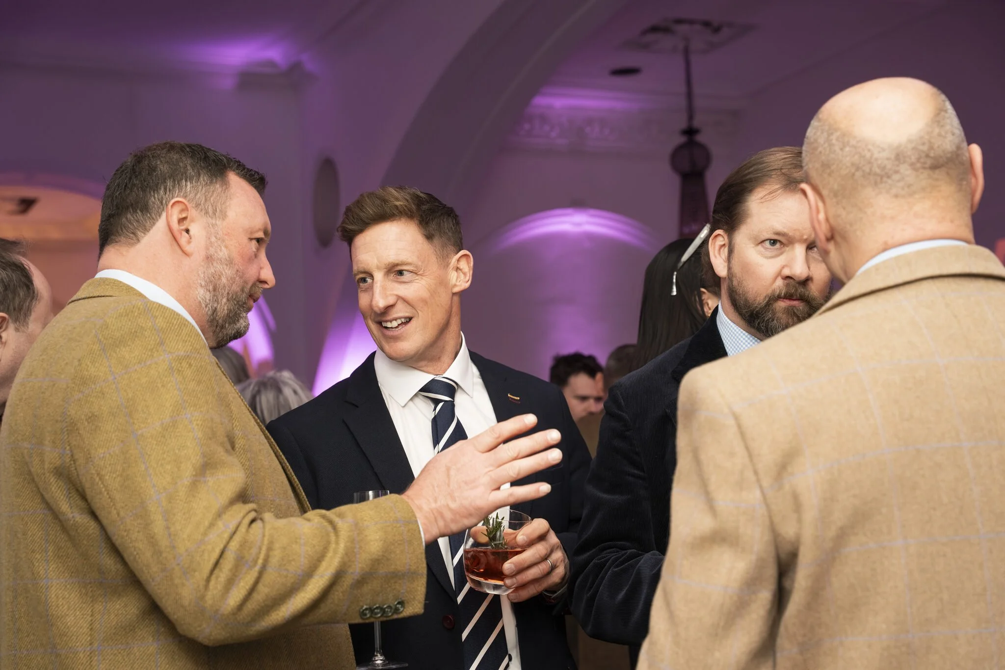 Group of men engaged in conversation at an indoor event, with purple lighting and elegant decor.