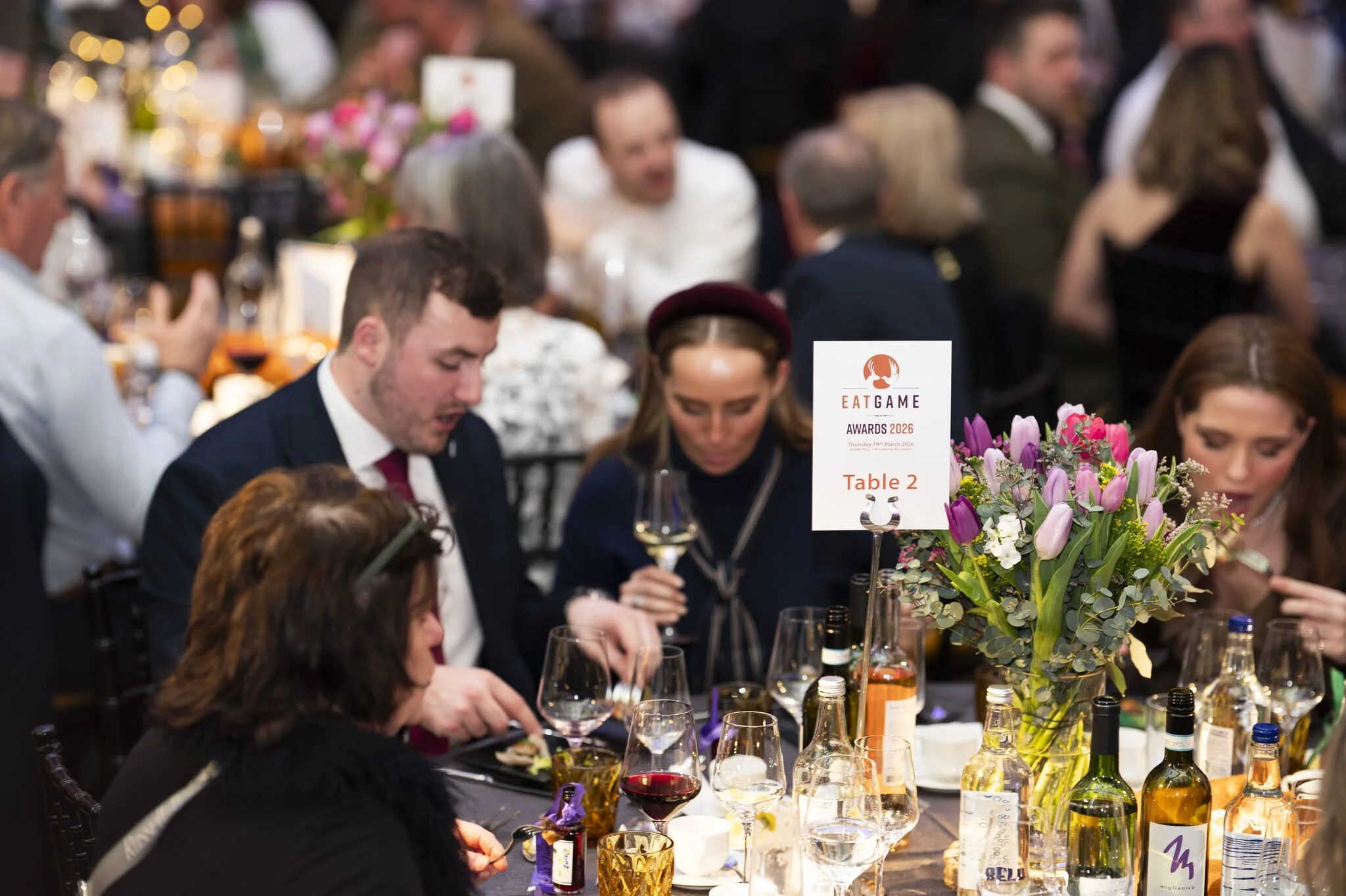 A group of people dressed in formal attire sitting around a table at an event, with a floral centerpiece and a sign indicating 'Eat Game Awards 2026, Table 2'.