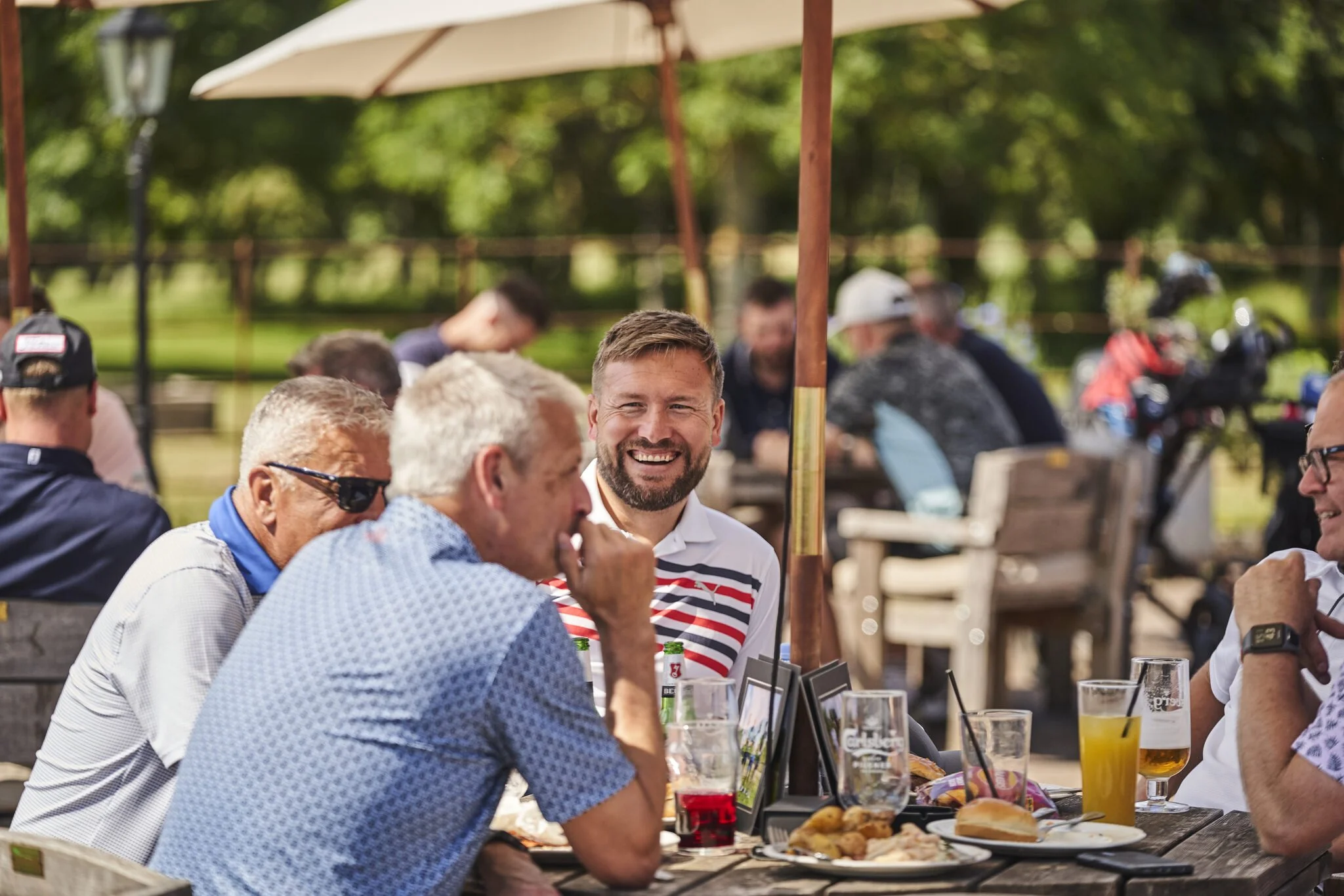 People enjoying a meal at an outdoor patio on a sunny day, with food and drinks on the table.