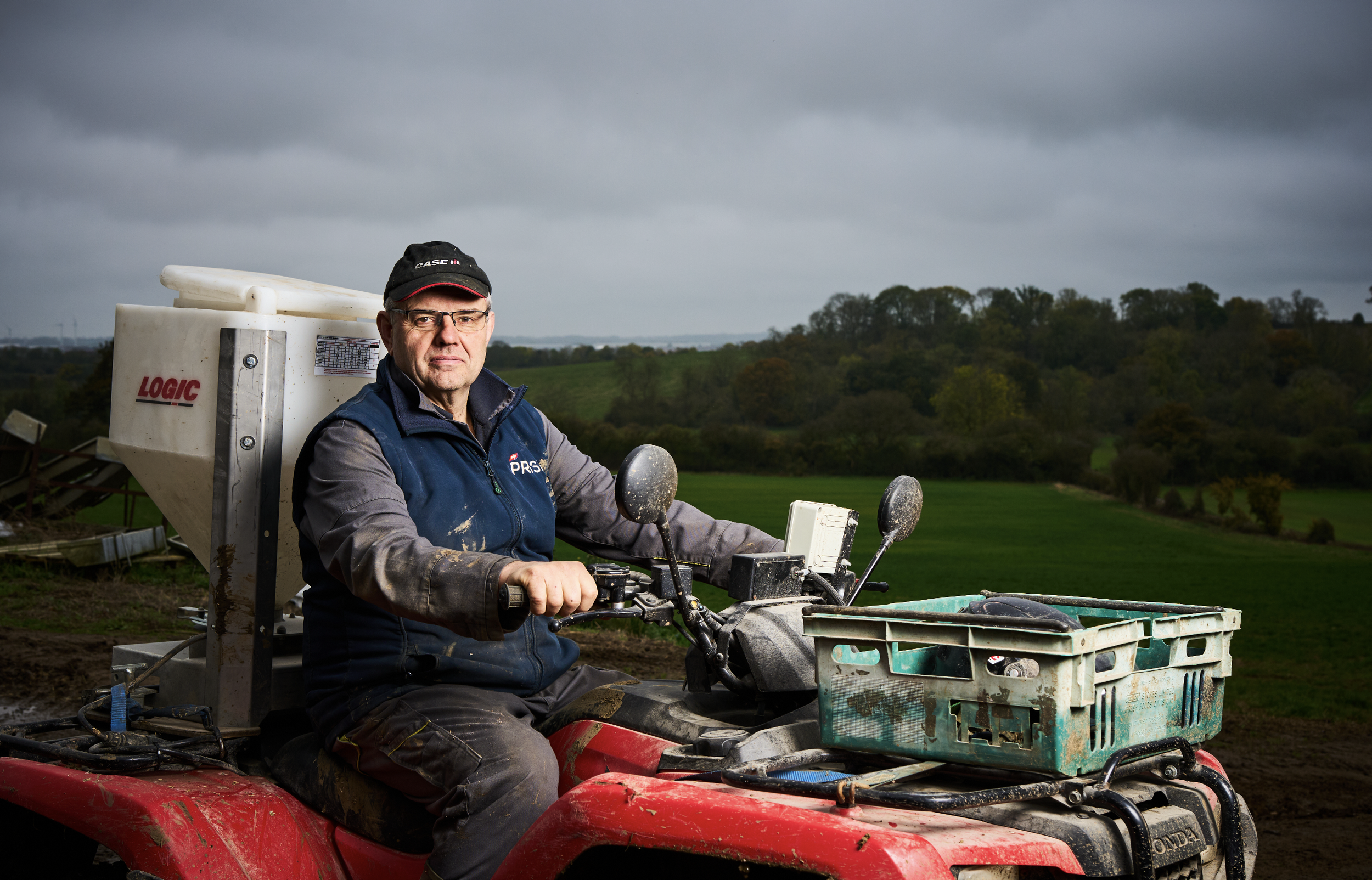 Farmer sits on a quad bike in a field. With Fertiliser spinner mounted on the back. 