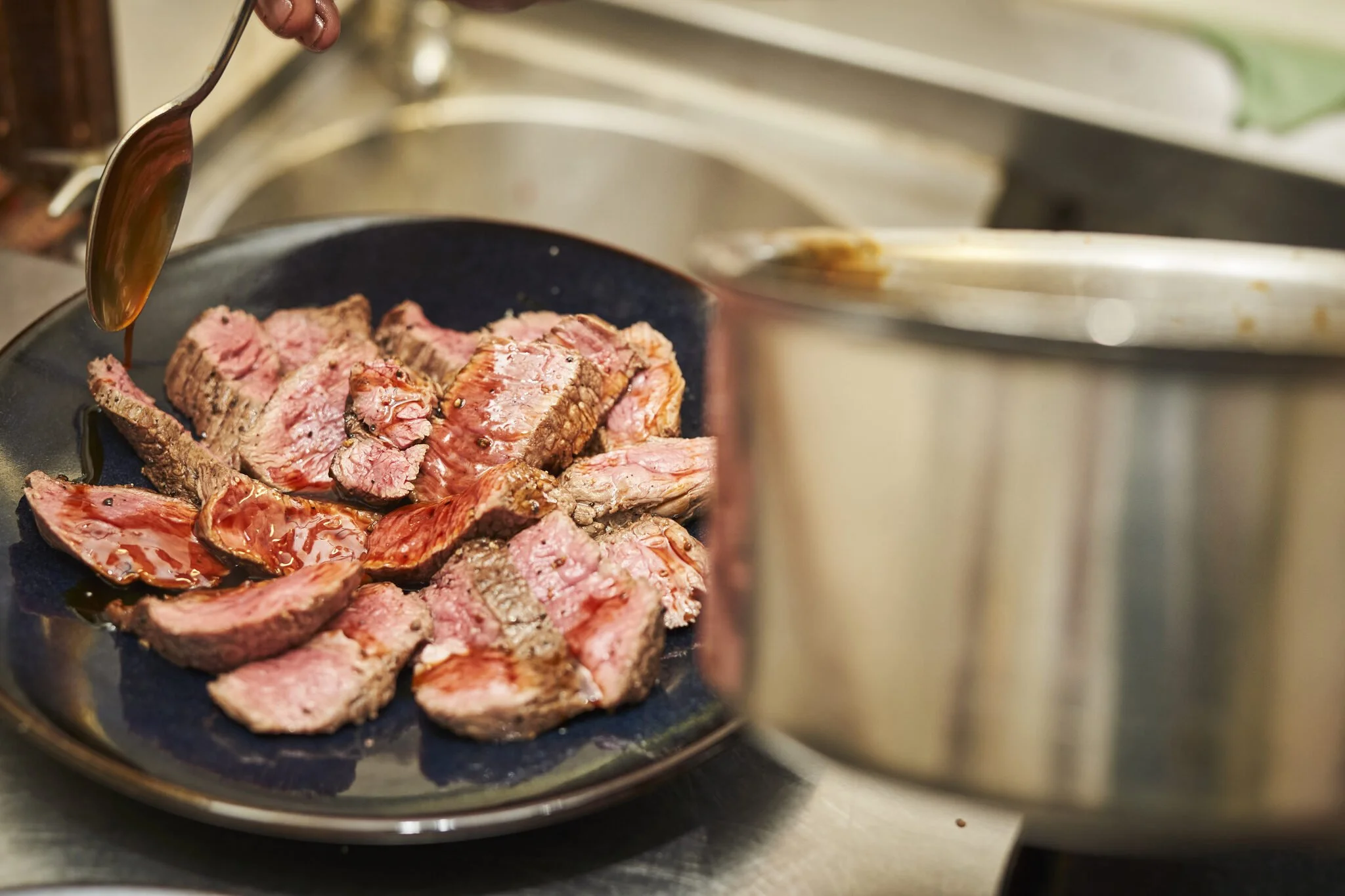 Slices of cooked steak on a black plate with gravy being poured over them.