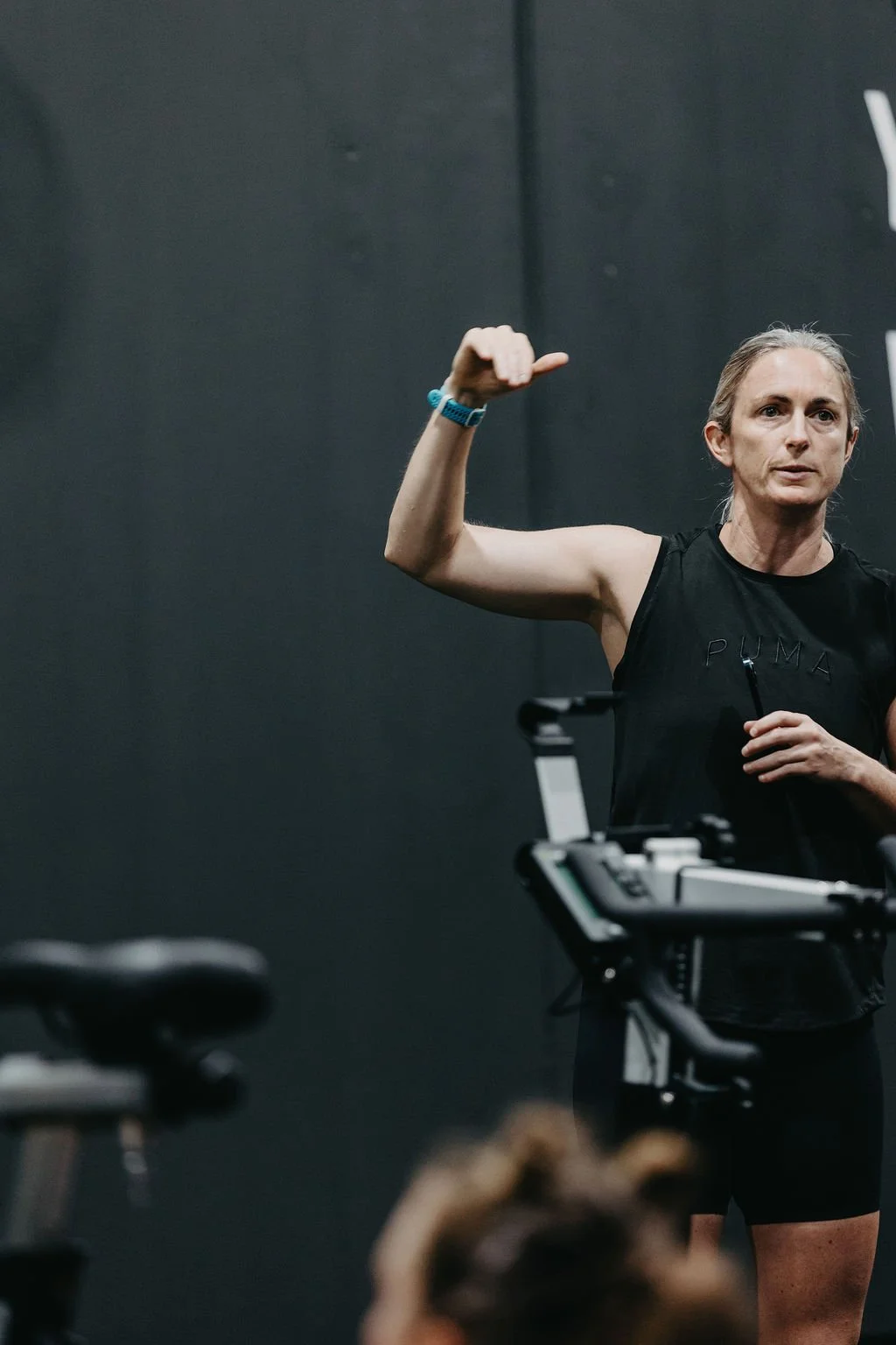 A woman in a black sleeveless shirt speaking to a group.
