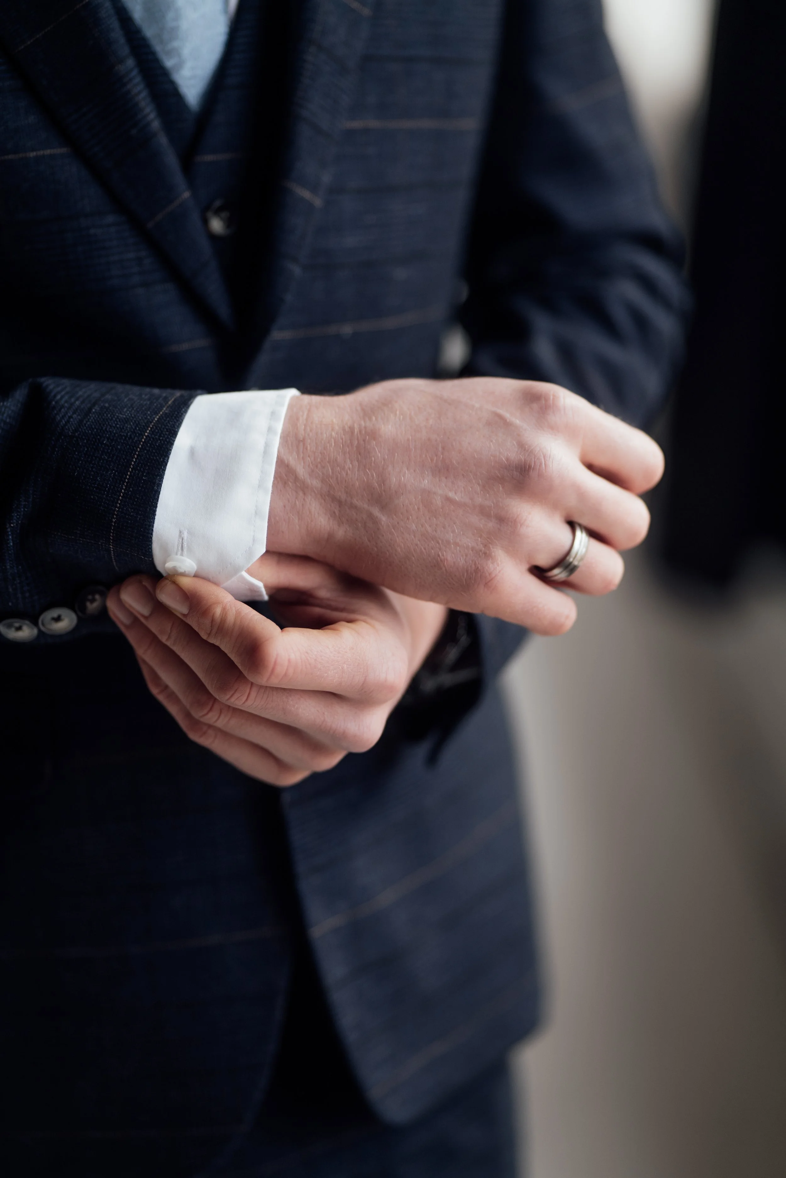 A person in a dark business suit adjusting their white cuffed shirt sleeve.