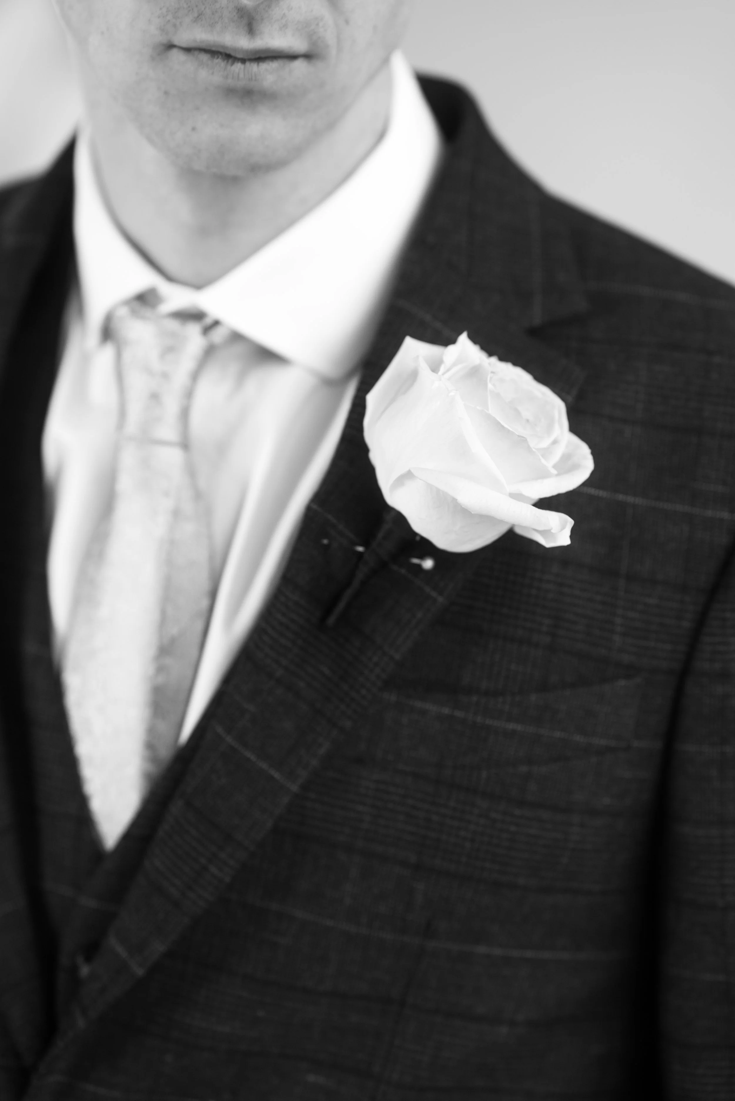 Close-up of a man's suit with a white flower pinned to the lapel, in black and white.