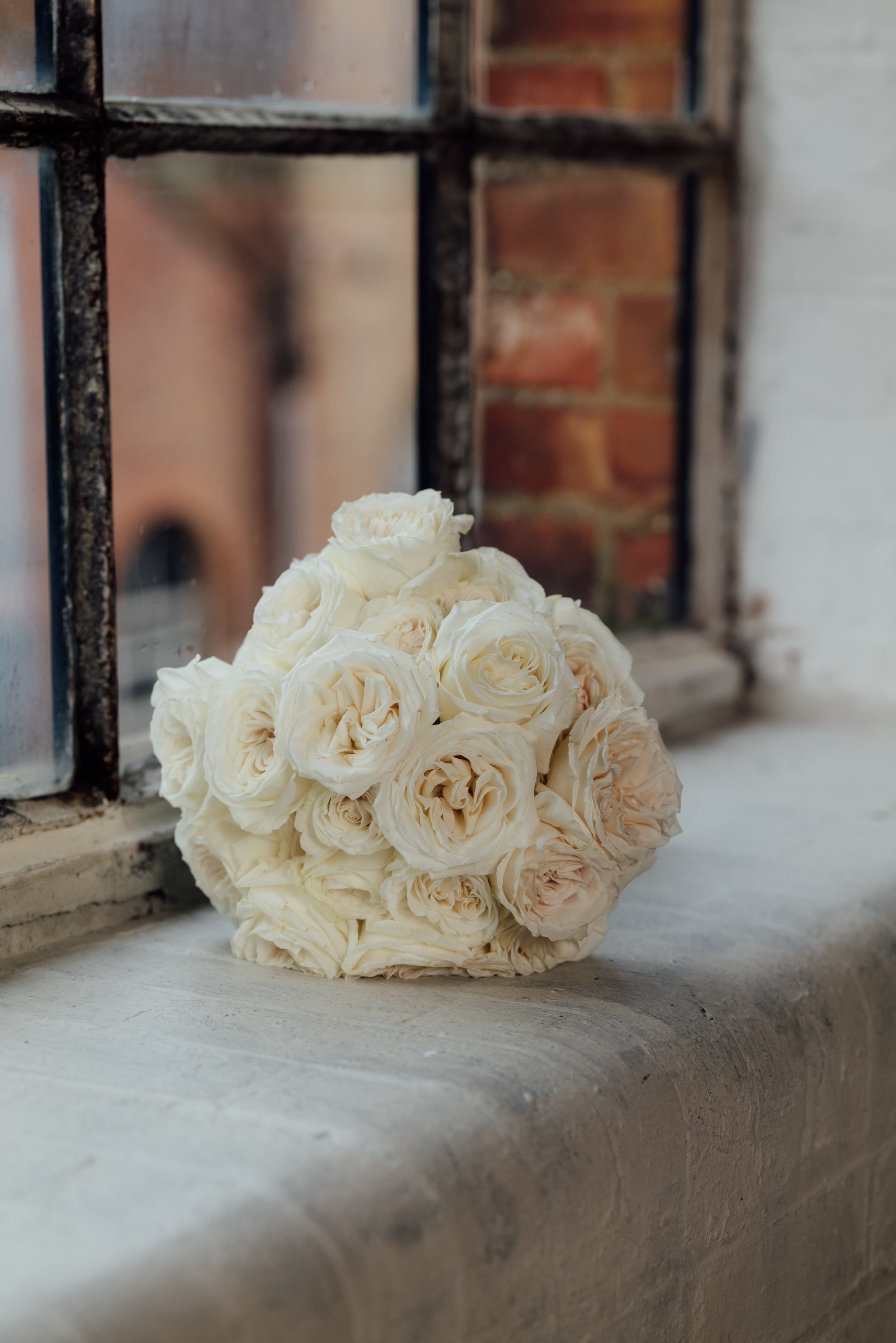 A bouquet of white roses resting on a windowsill with an iron window grate and a brick wall in the background.