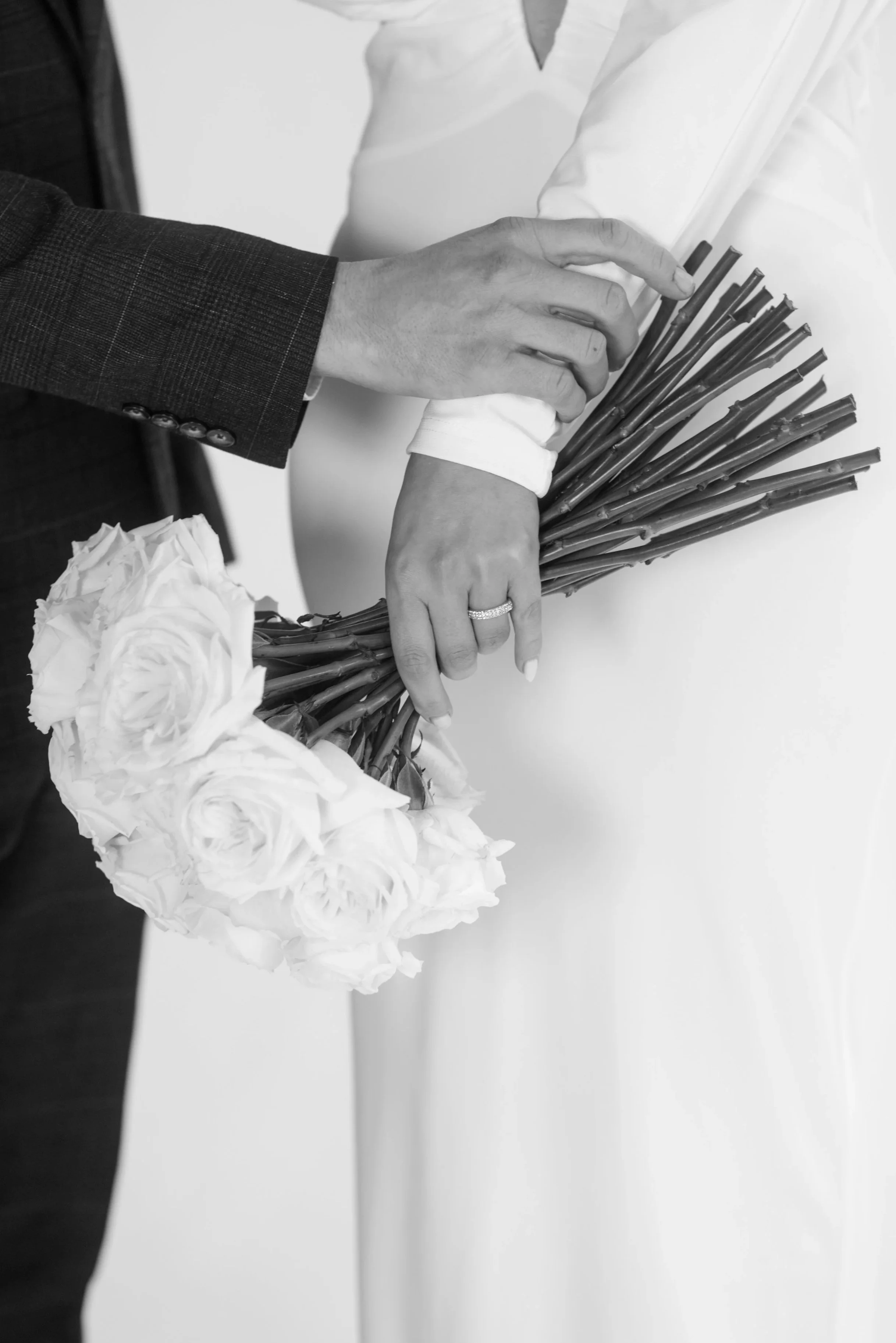 A couple holding a bouquet of roses, with the bride wearing a wedding ring, in a black and white photo.