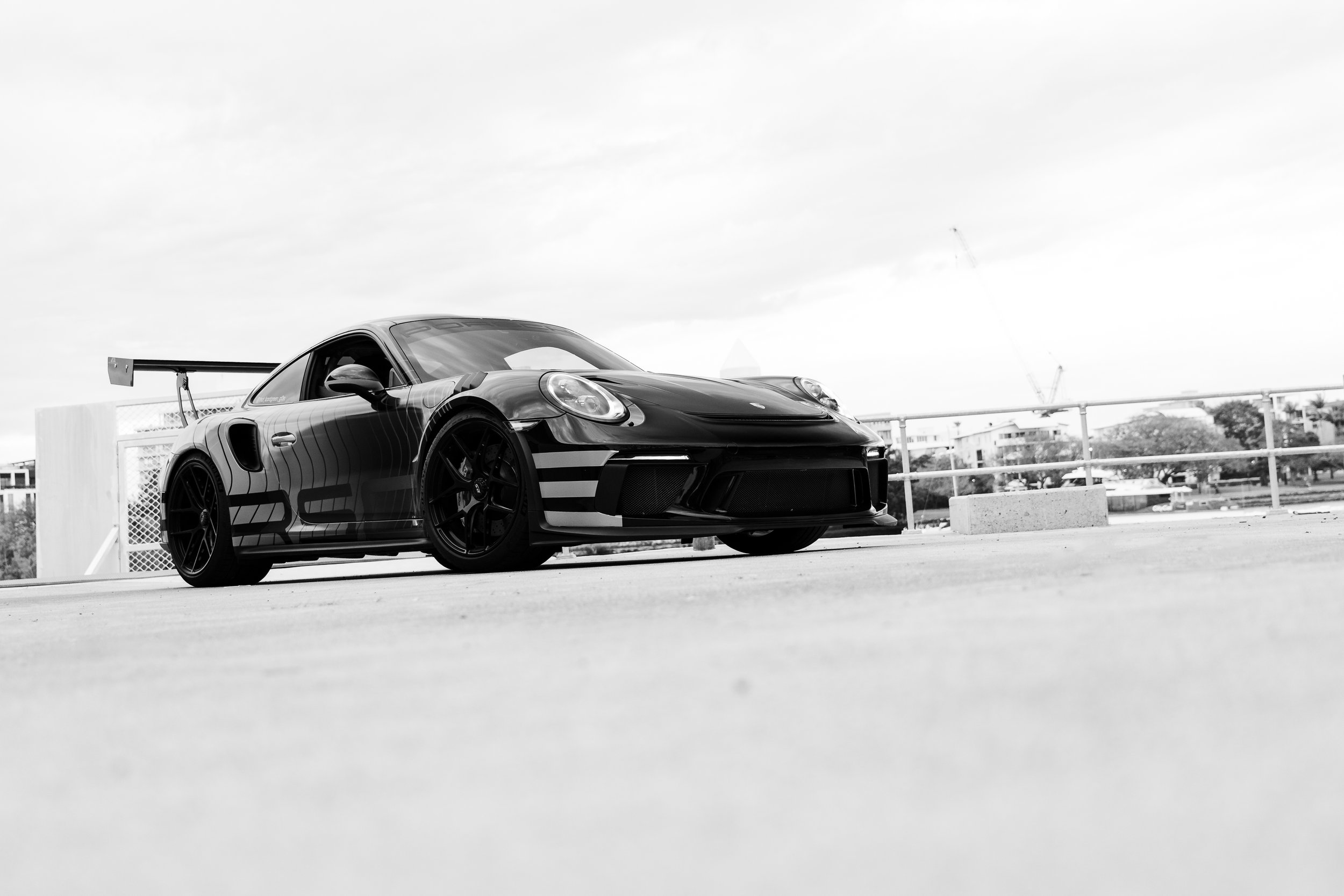 A black sports car with racing stripes parked on an outdoor rooftop parking lot.