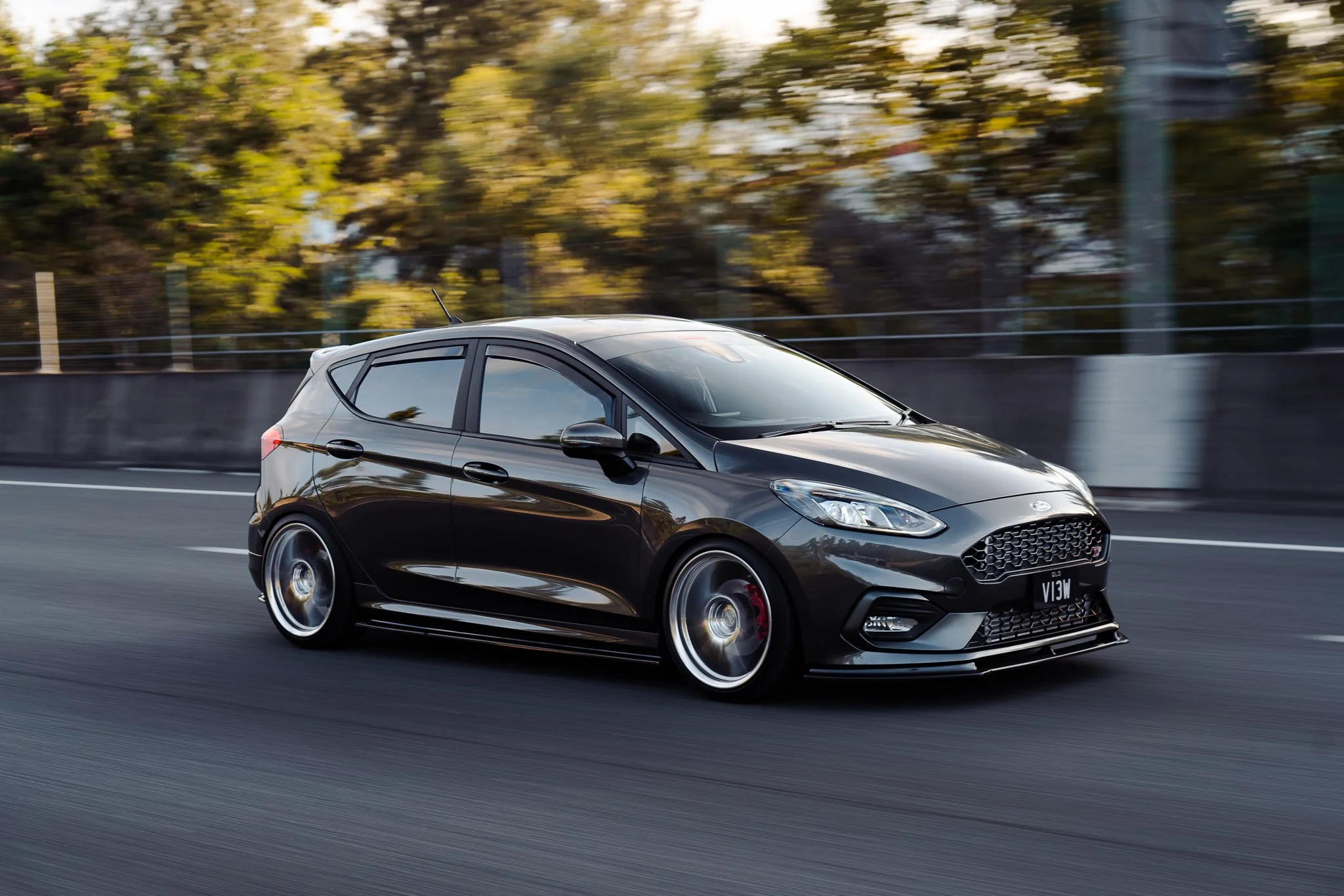 Black Ford Fiesta driving on a highway with trees in the background.