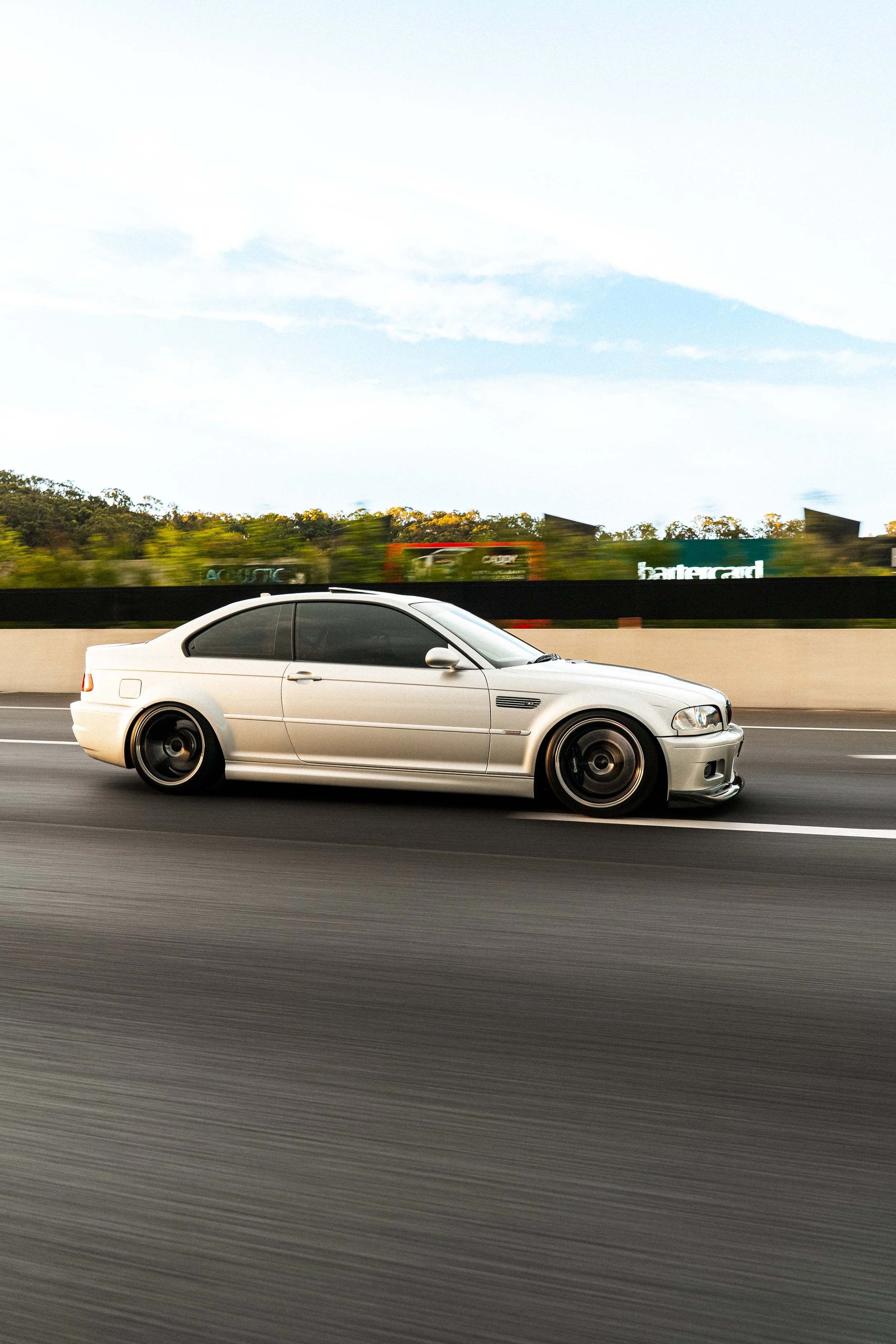 Silver sports coupe car driving on highway with motion blur background and partly cloudy sky.