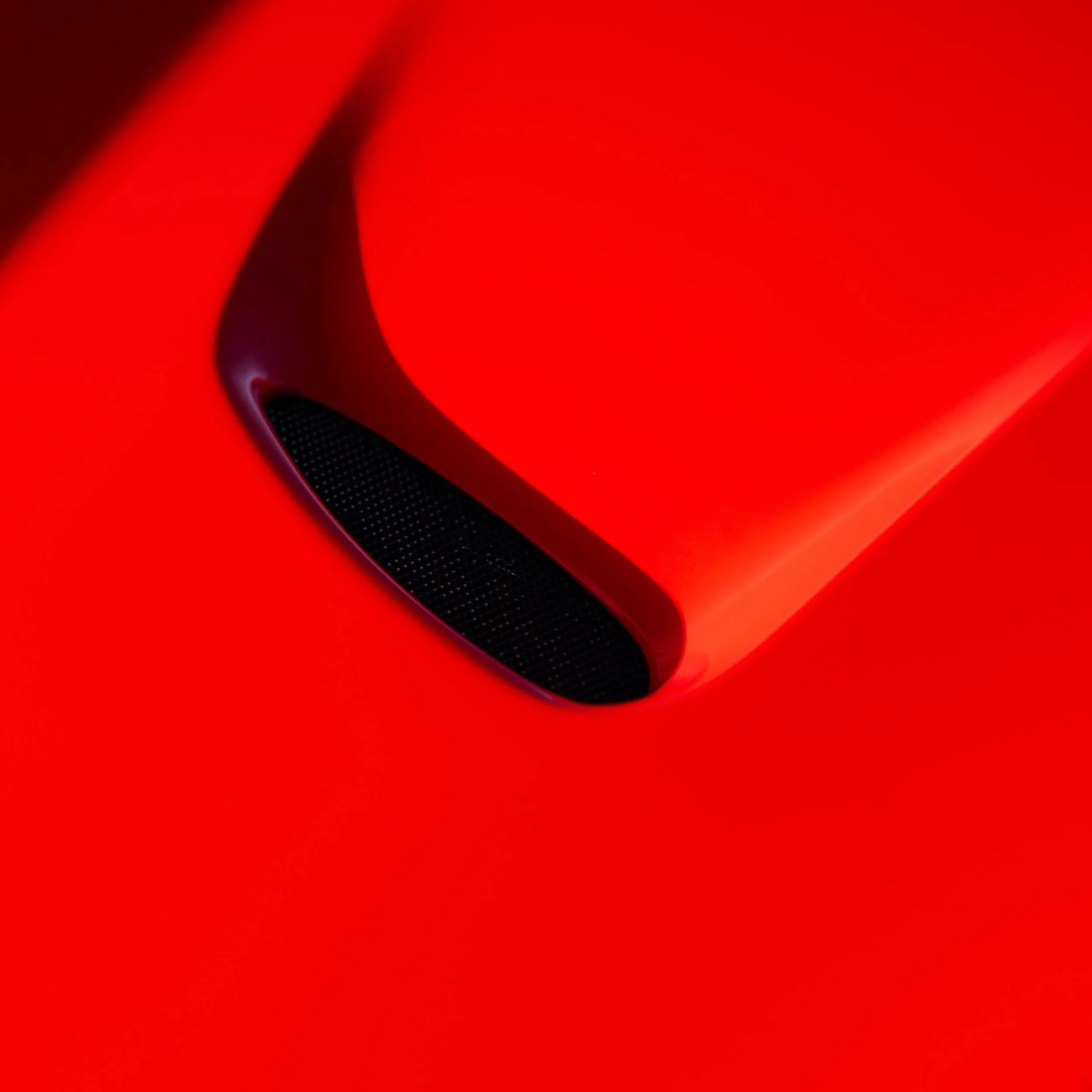Close-up of a red sports car hood vent with black mesh detail.