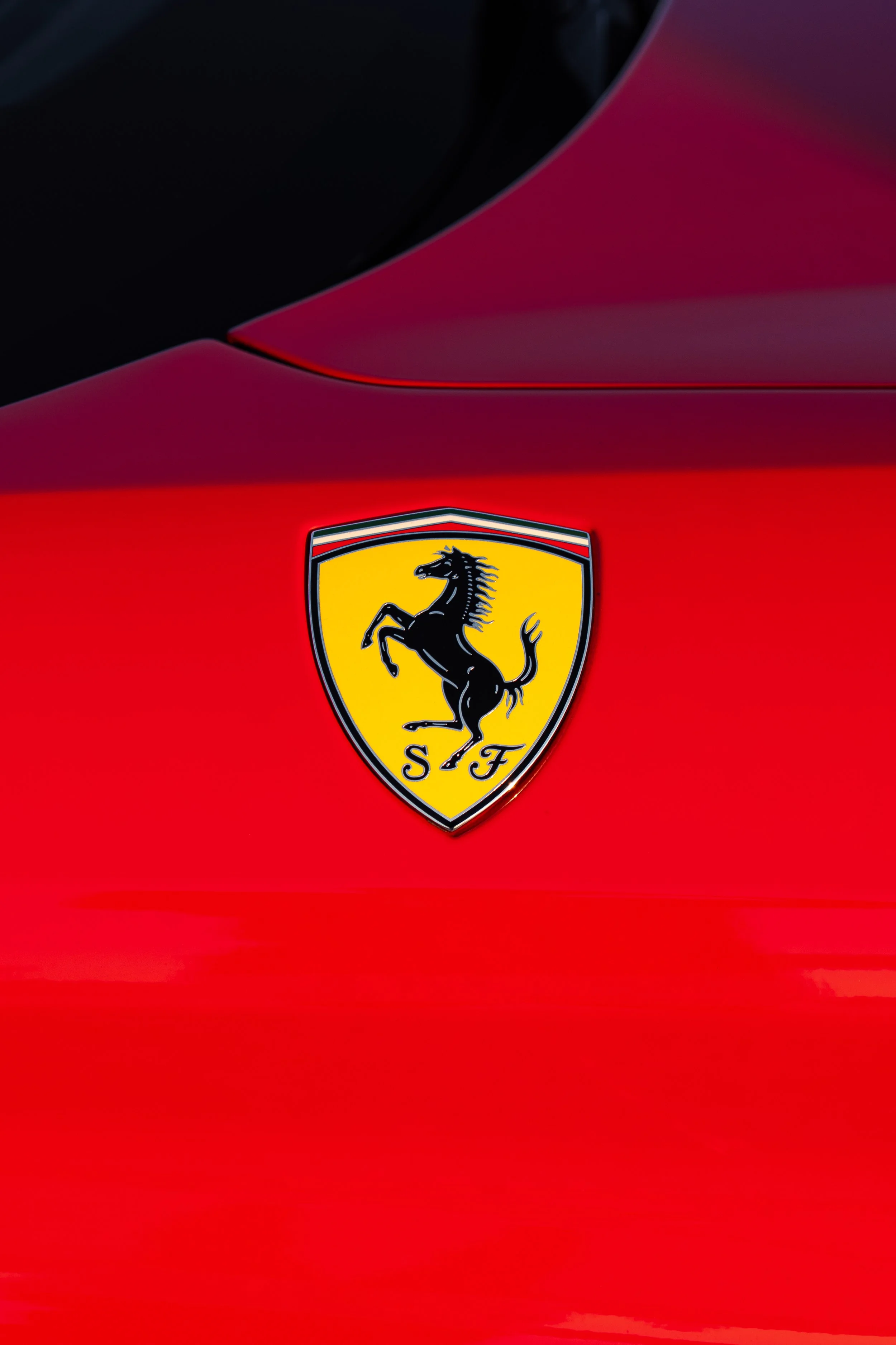Close-up of a Ferrari logo on a red car's hood, with a black part near the top of the image.