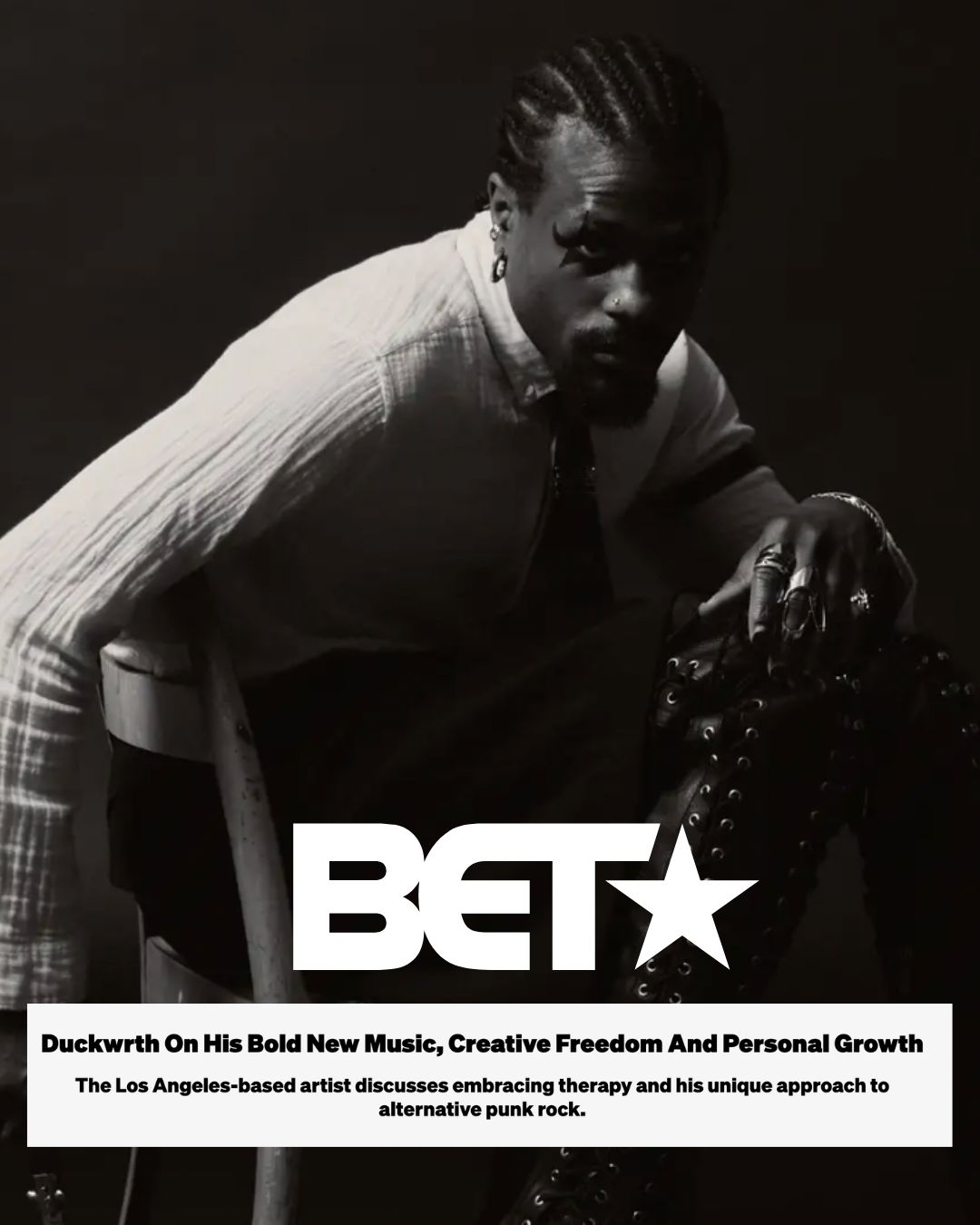 Black and white photo of a man with braided hair and multiple rings, sitting on a stool with his hand resting on his knee, next to a BET magazine cover.