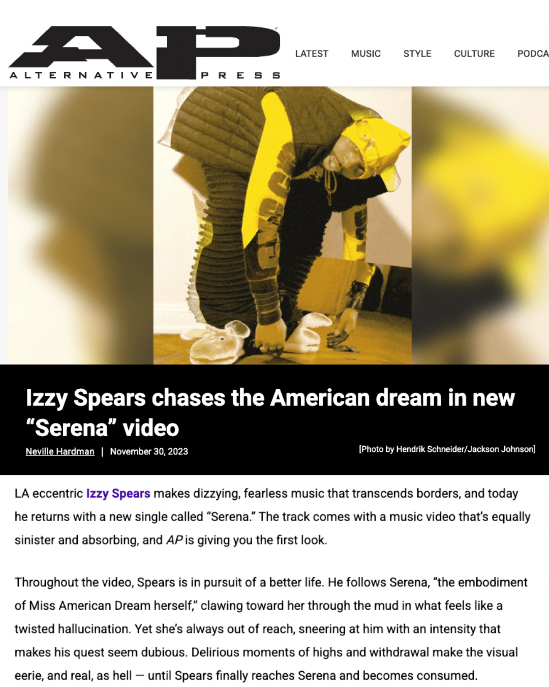 Screenshot of an online news article about Izzy Spears' new music video for the song 'Serena,' featuring a person dressed in a yellow and black costume with animal-like aspects, possibly in a performance or artistic setting.