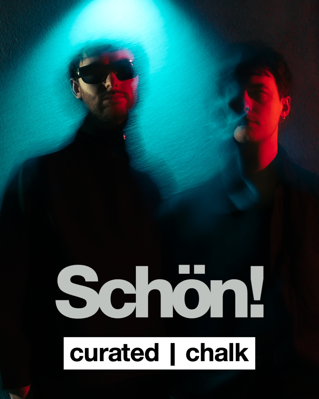 Two people in a dark room illuminated by blue and red neon lights, one wearing sunglasses and a black turtleneck, the other with short hair and earrings, with the word 'schön!' and 'curated | chalk' written on the image.