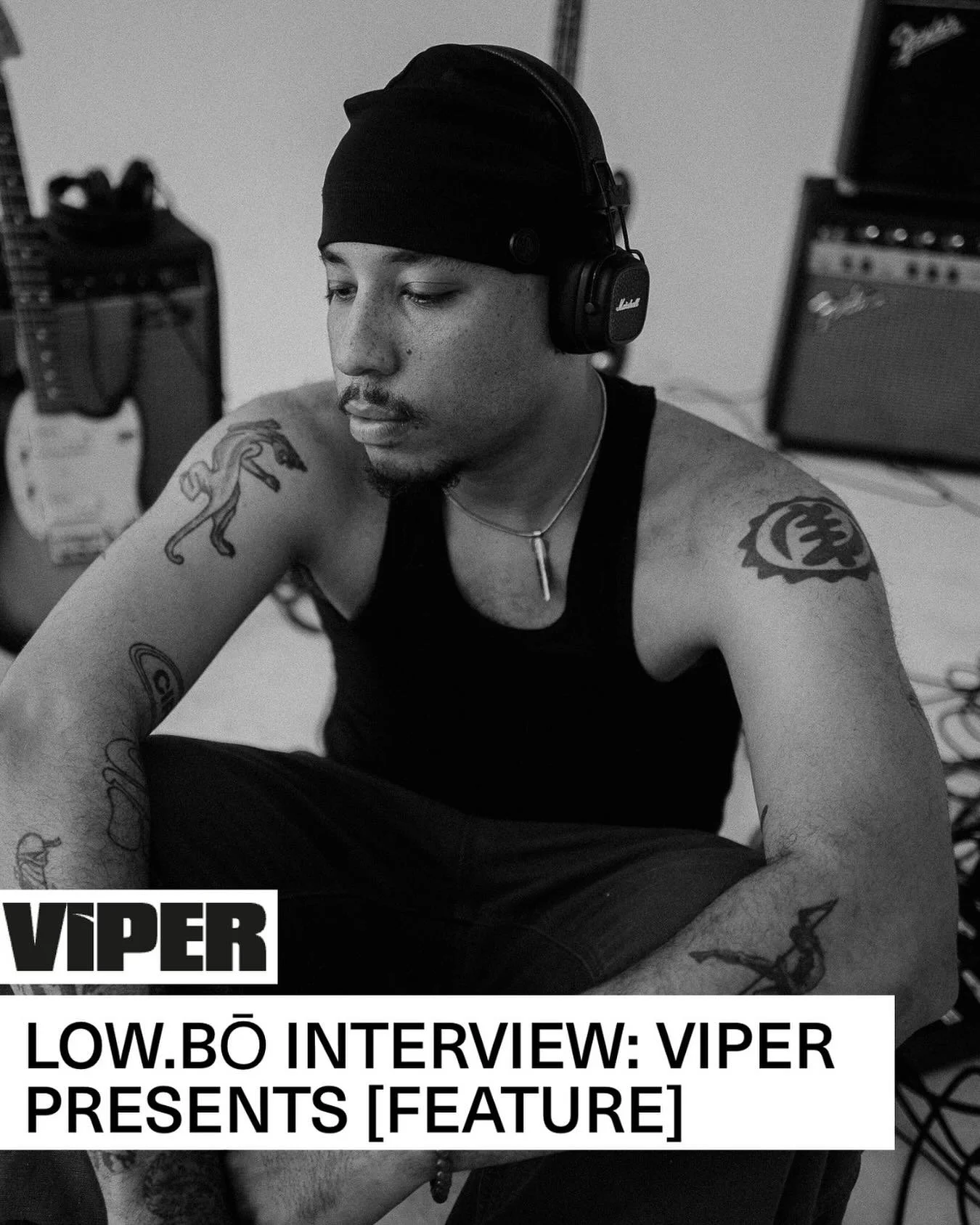 A young man with tattoos, wearing a black tank top, a black beanie, and headphones, sitting in a music studio with audio equipment in the background. The image has a label that reads 'VIPER LOW.BØ INTERVIEW: VIPER PRESENTS [FEATURE]'.