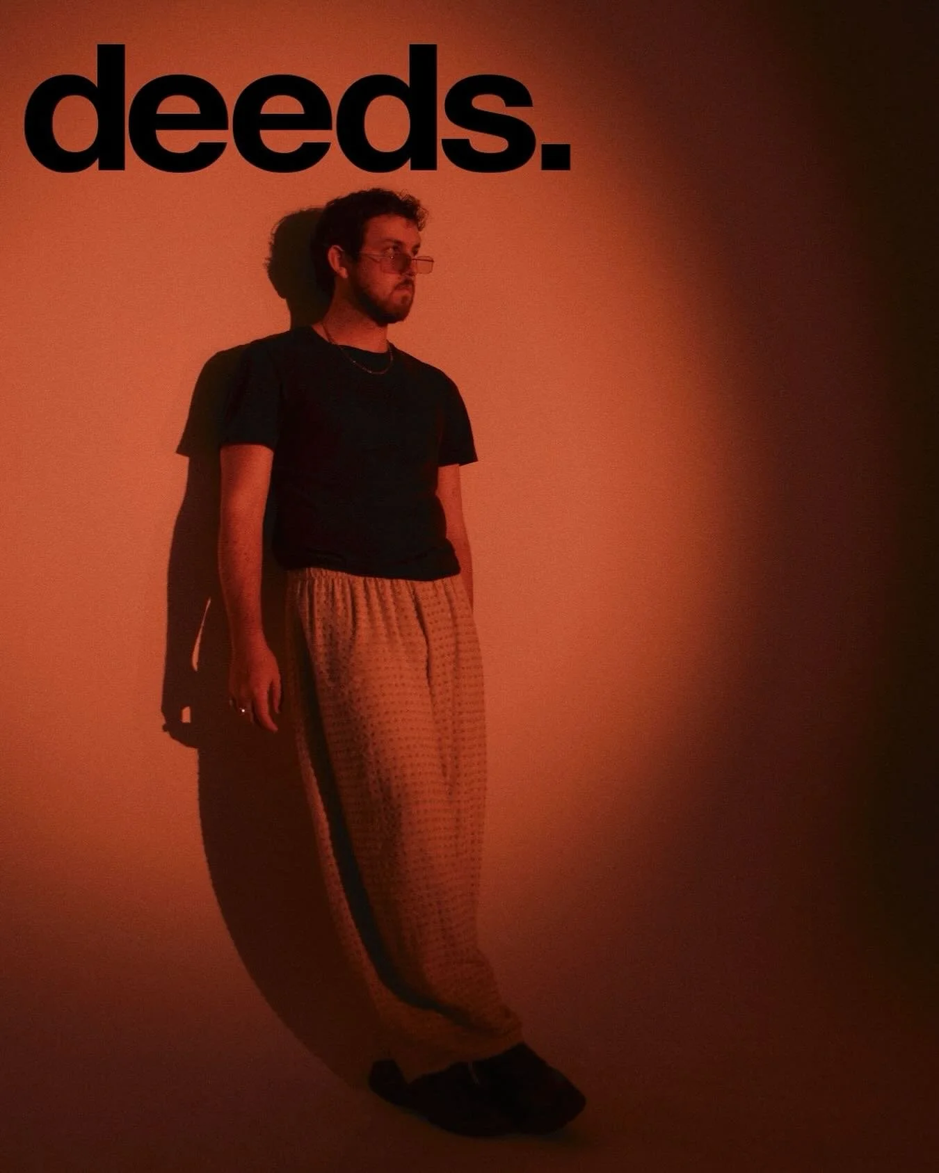A man standing against a plain wall with the word 'deed' in bold black letters above his head, casting a shadow.