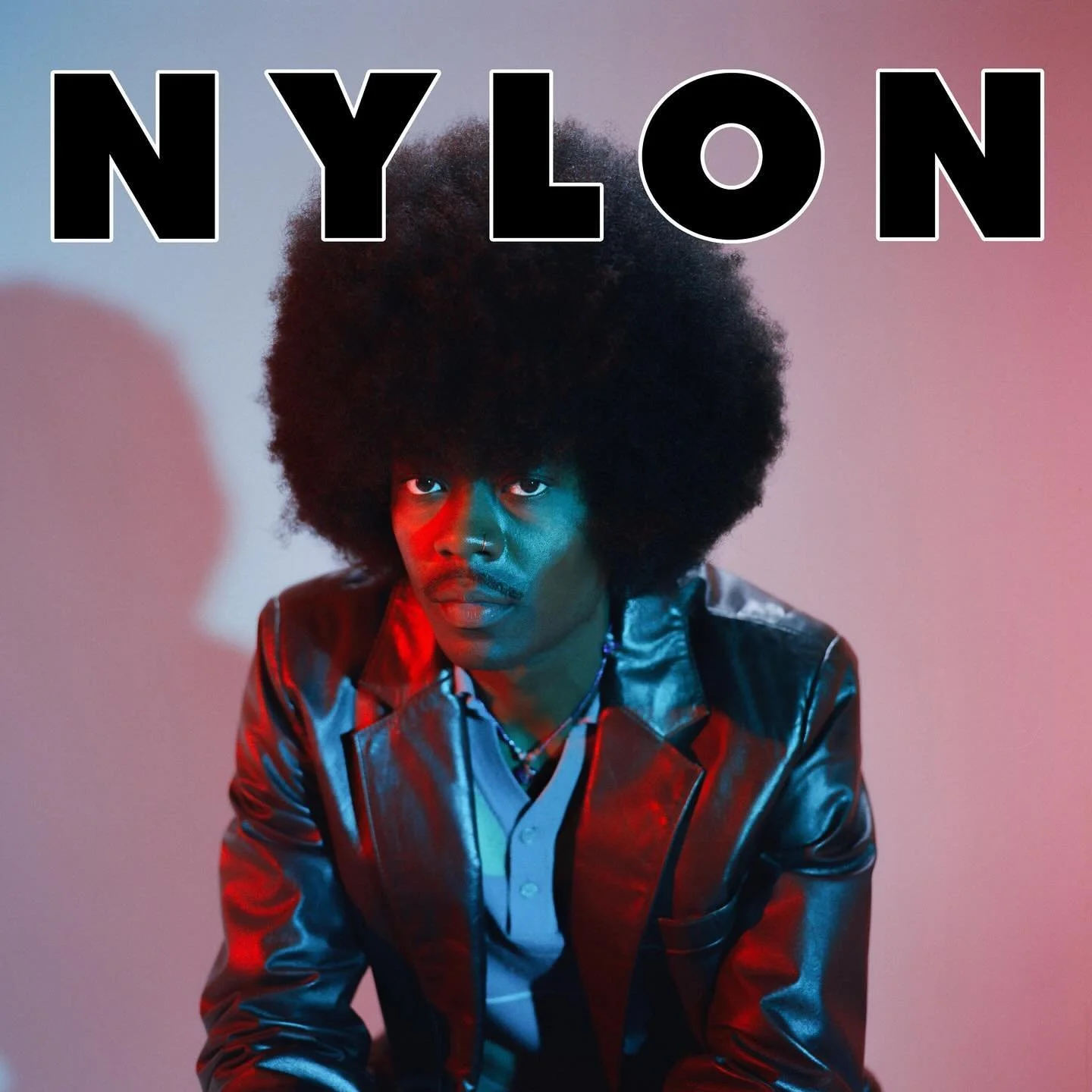 Portrait of a person with a large afro hairstyle, wearing a shiny leather jacket and a white shirt, with colorful lighting in the background.